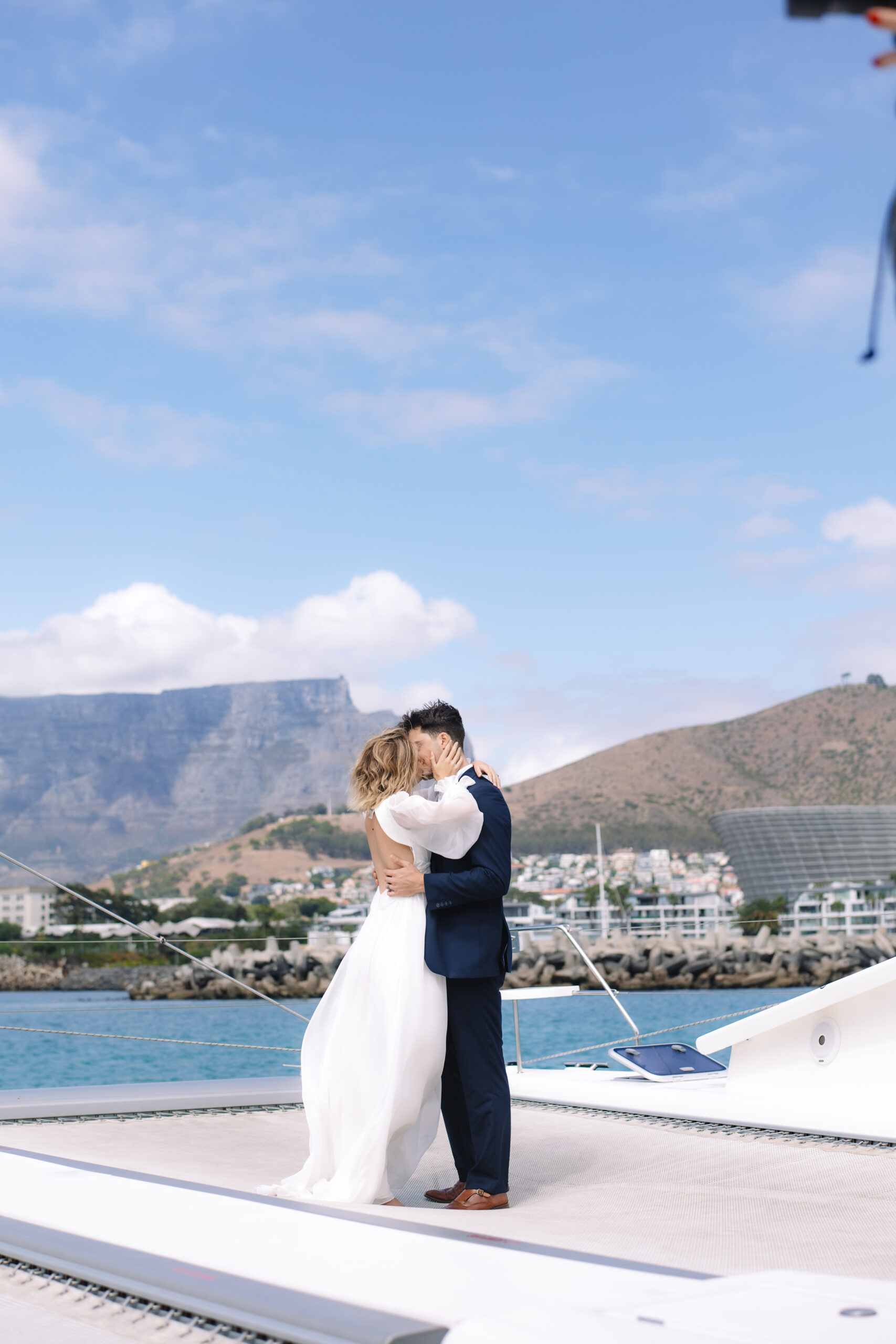 Romantic Cape Town elopement moment of a bride and groom embracing on a sailboat, with Table Mountain and the city skyline in the background.