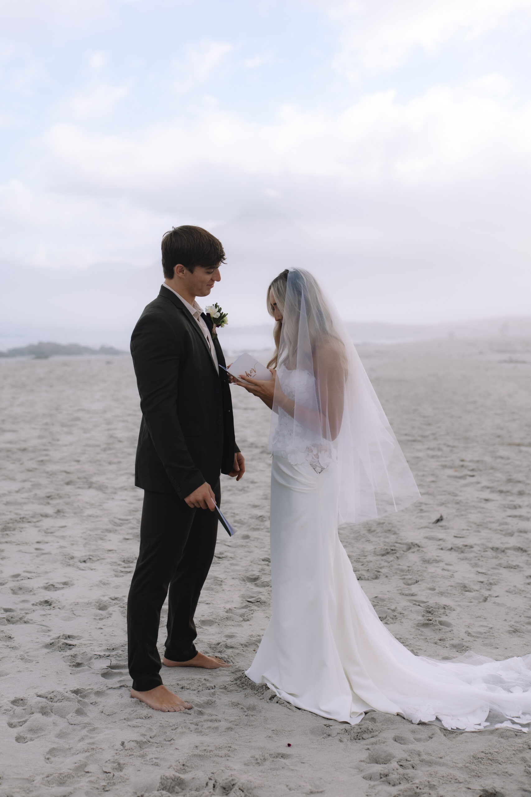 Intimate Cape Town elopement ceremony on a quiet beach, with the bride and groom standing barefoot in the sand as they exchange vows in soft coastal light.