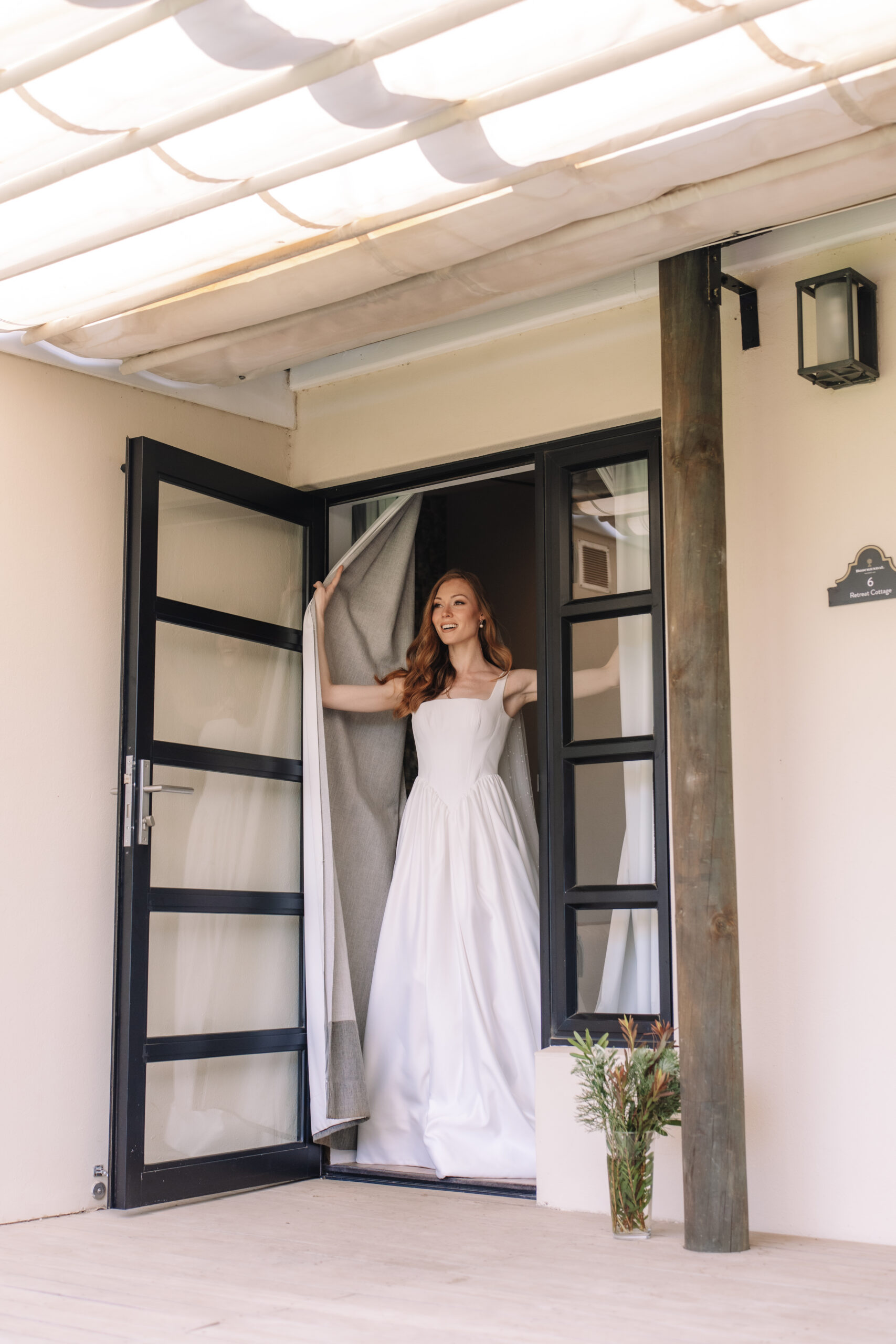 Bride in a minimalist white gown standing in a modern villa doorway near Cape Town.