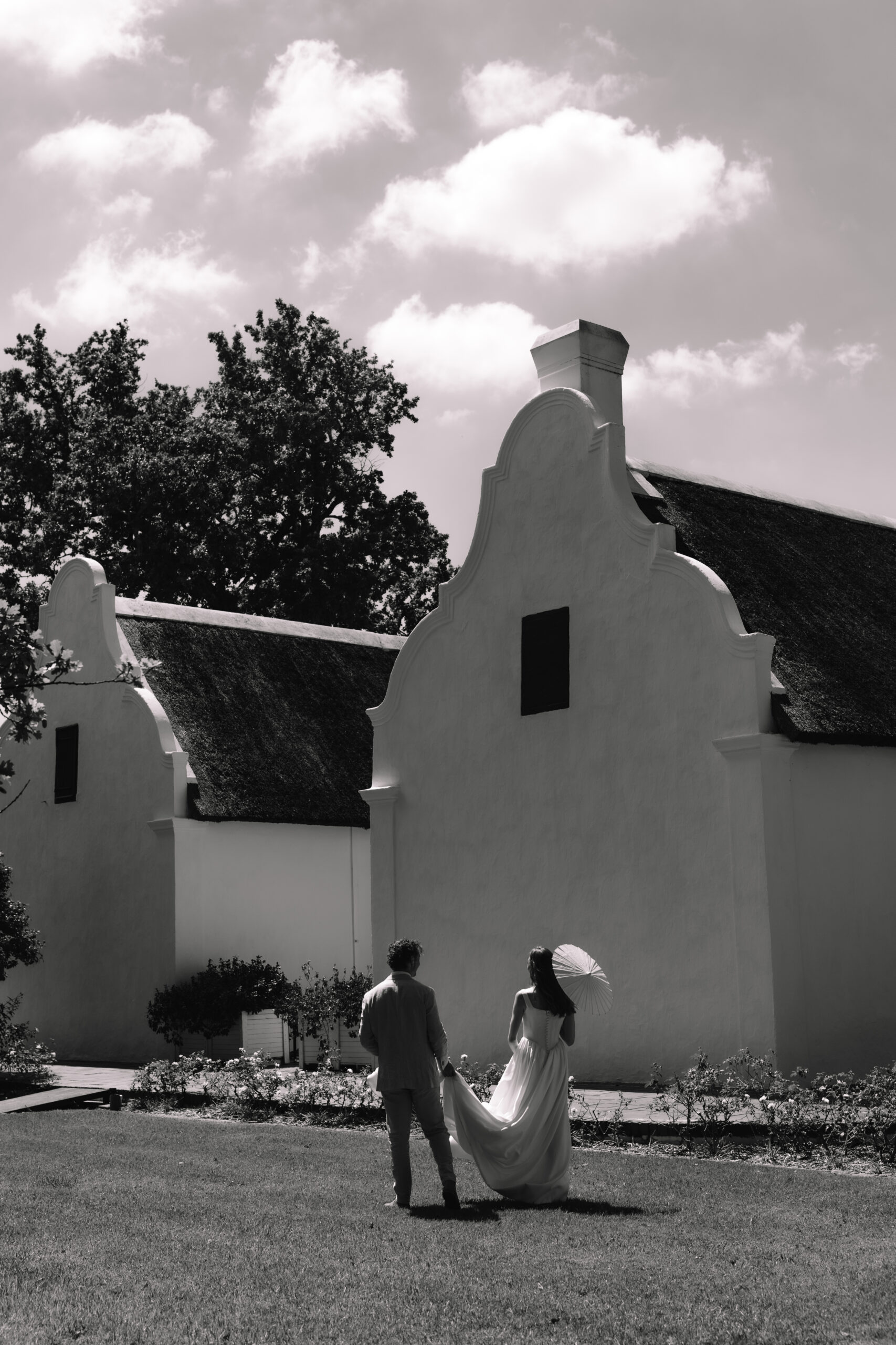 Newlyweds walking across lawn in front of Cape Dutch architecture at cape town wedding locations.