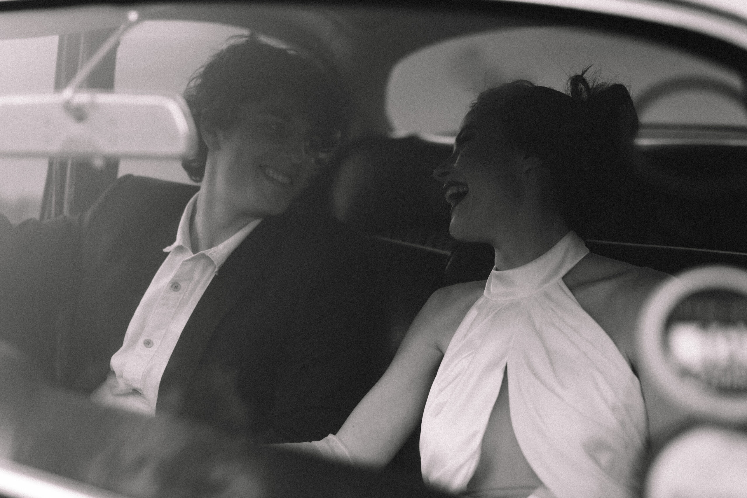 Black and white candid of newlyweds laughing inside a vintage car after their ceremony.