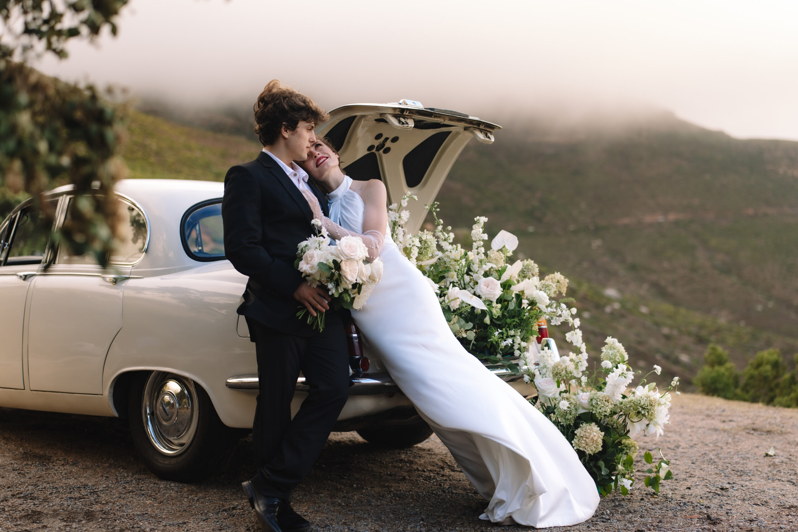 Elegant couple leaning against vintage car with mountain backdrop at scenic cape town wedding locations.