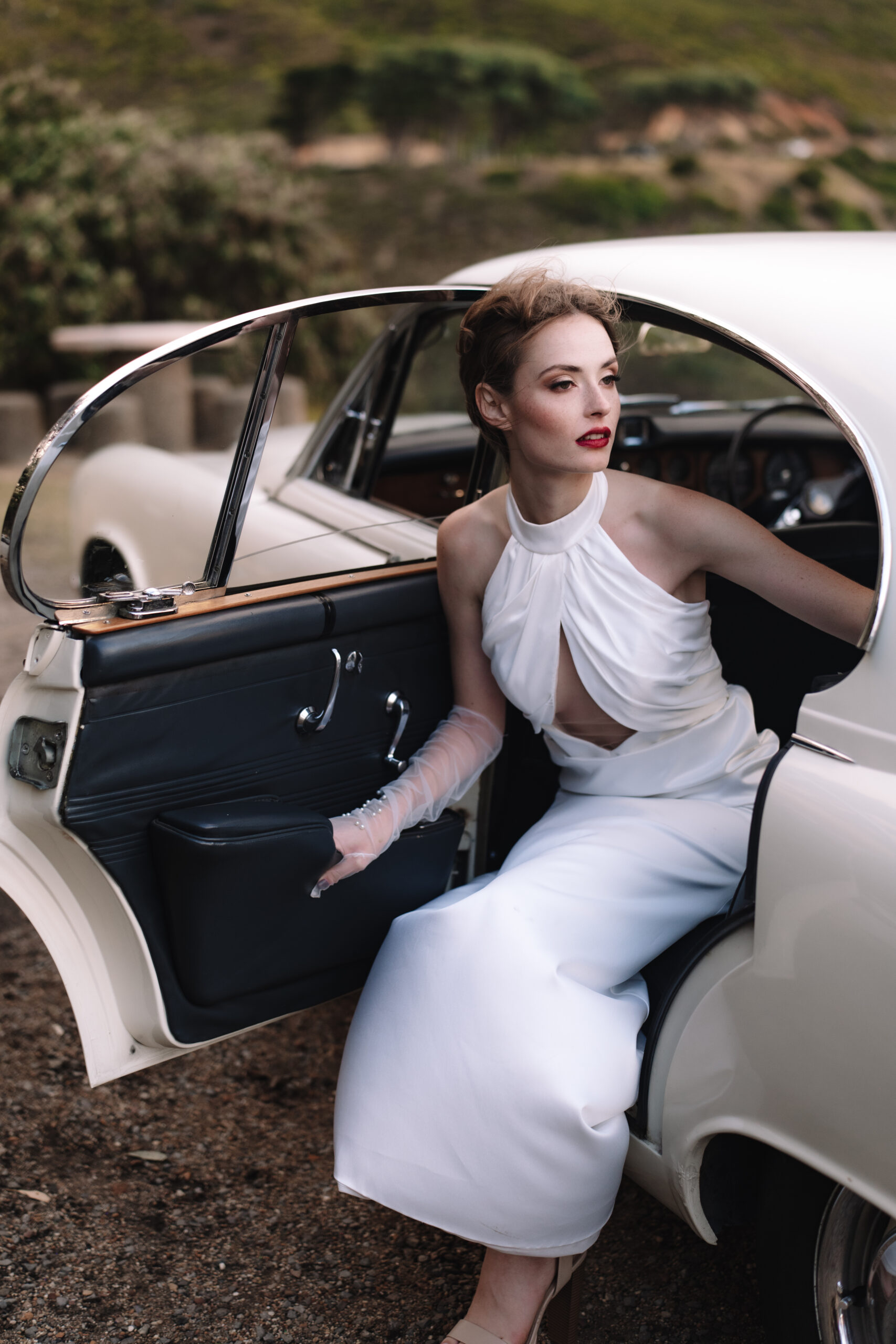 Bride stepping out of vintage car in sleek gown at scenic cape town wedding locations.