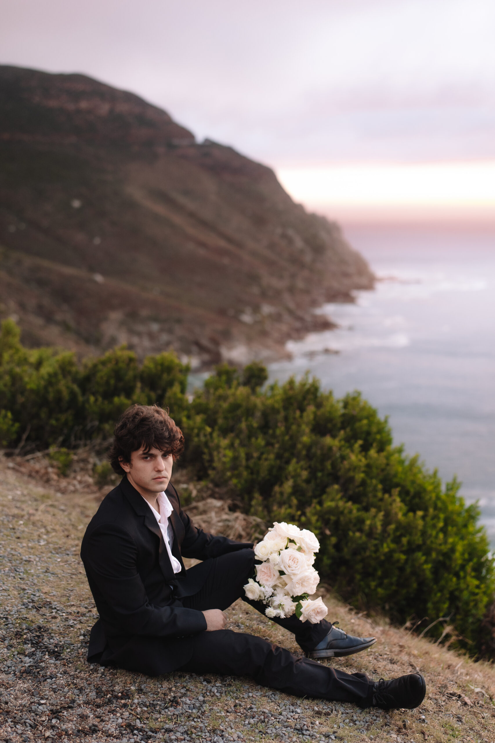 Groom seated on coastal cliffs overlooking the ocean at dramatic cape town wedding locations.