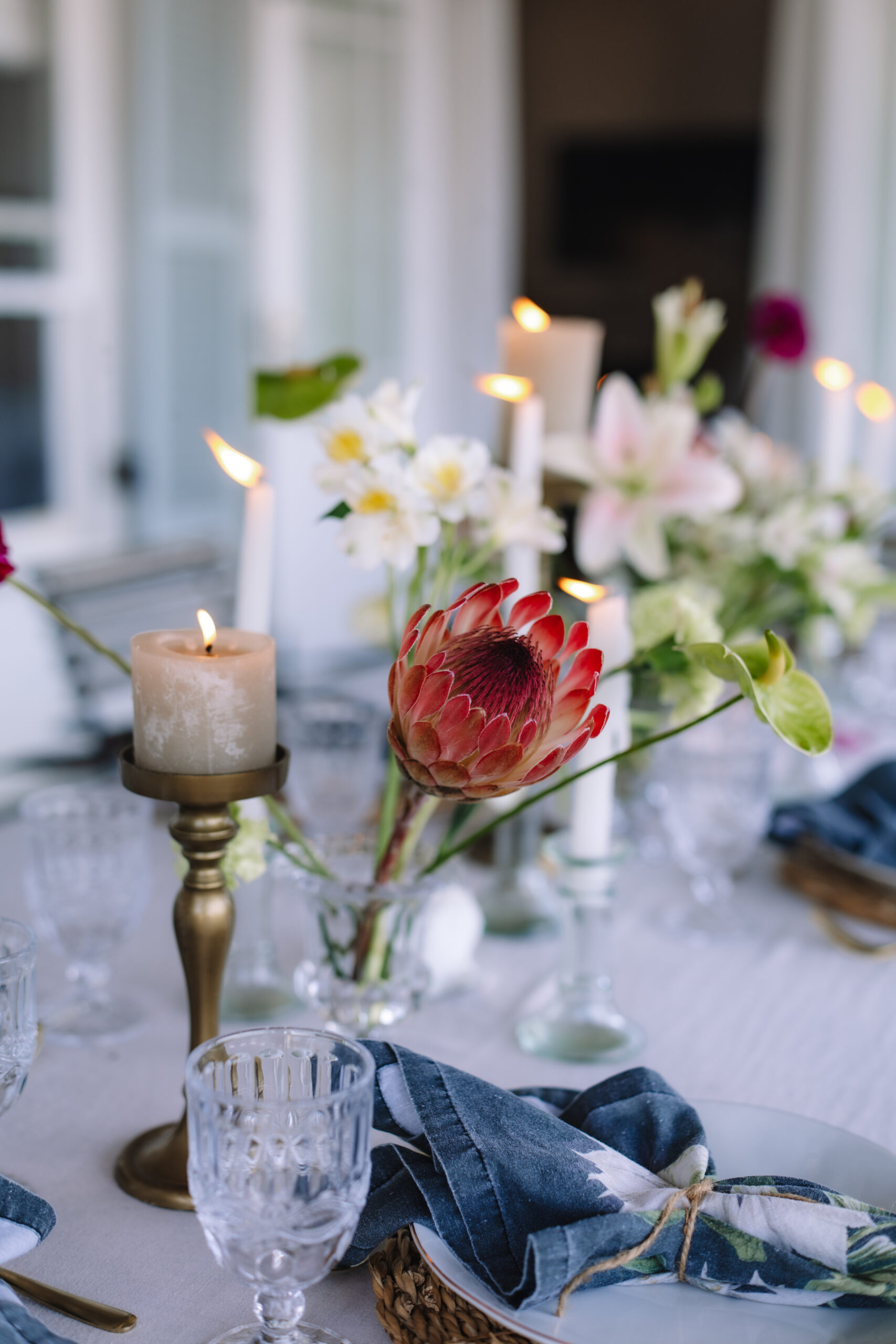 Elegant reception table with protea centerpiece, candles, and glassware at vineyard estate.