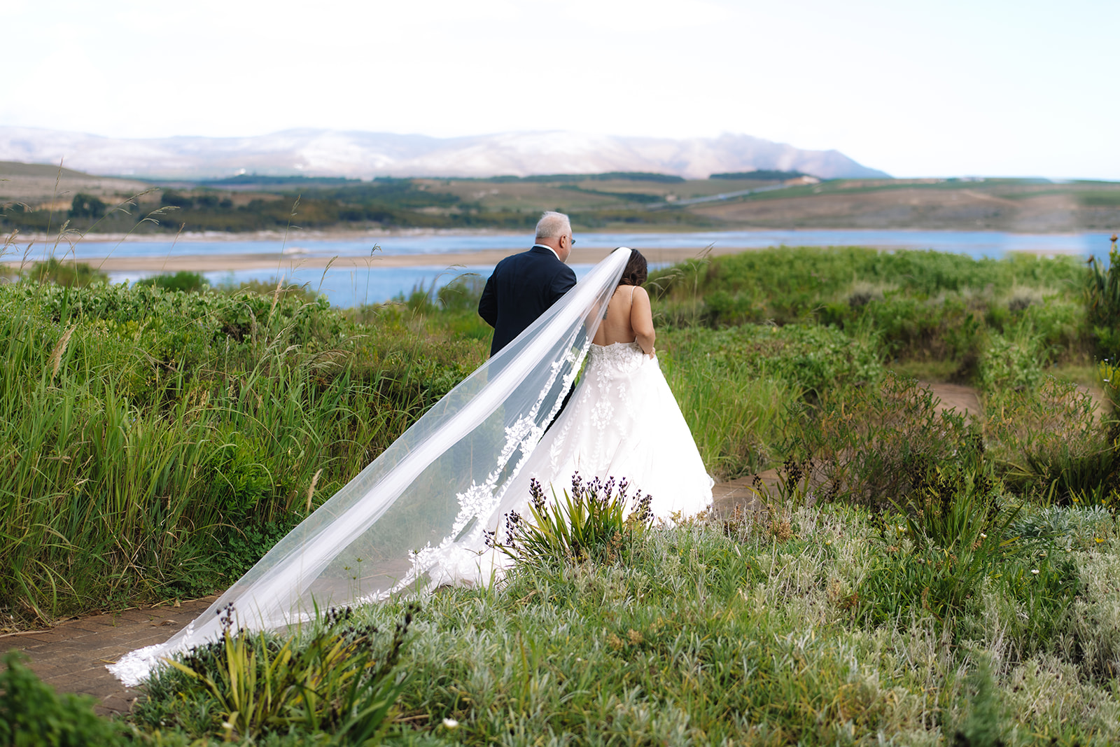 Newly married couple walking hand in hand through tall green grass after intimate elopement in South Africa.