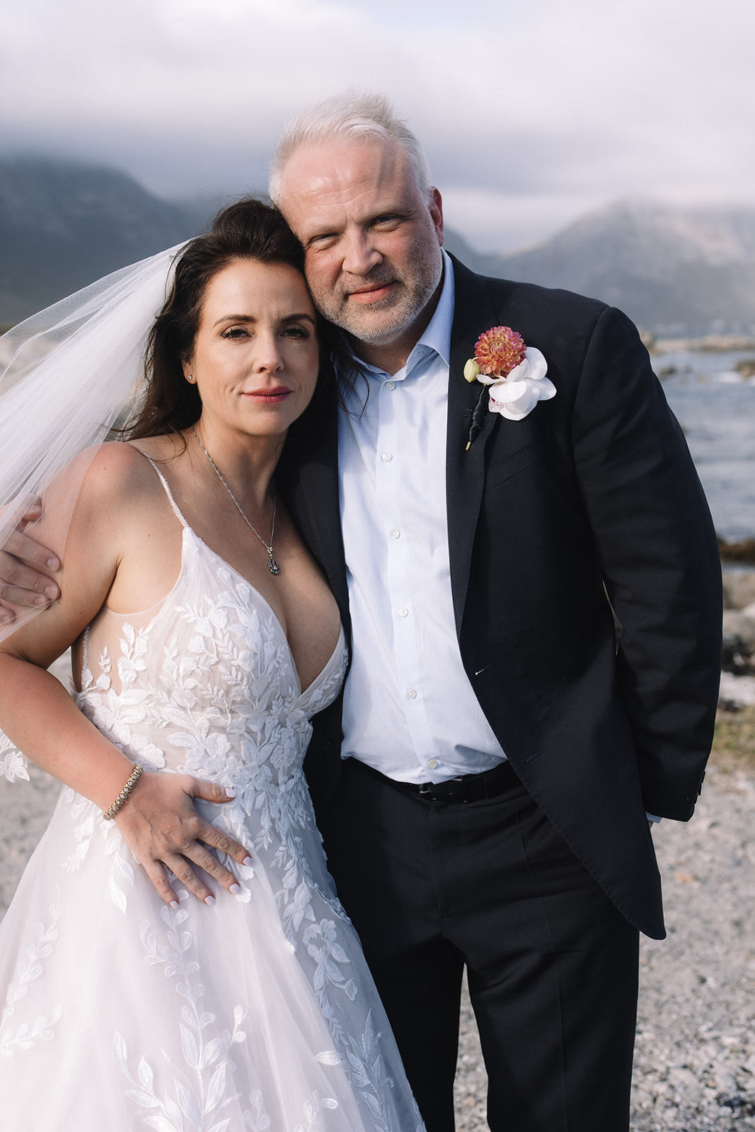 Bride and groom embrace as wind blows bride's hair after Stony Point Nature Reserve wedding at Betty's Bay.