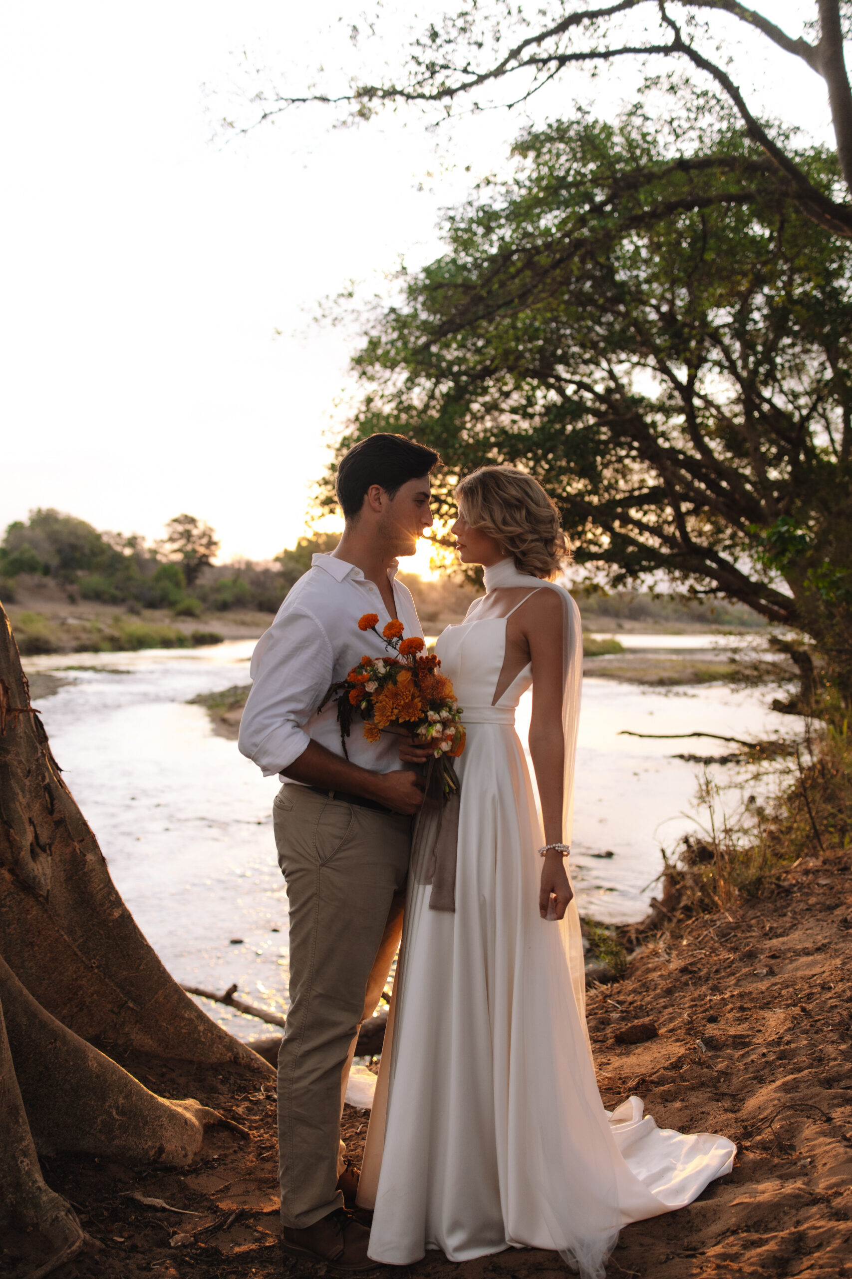 Bride and groom standing by a river at sunset during their Cape Town honeymoon safari.