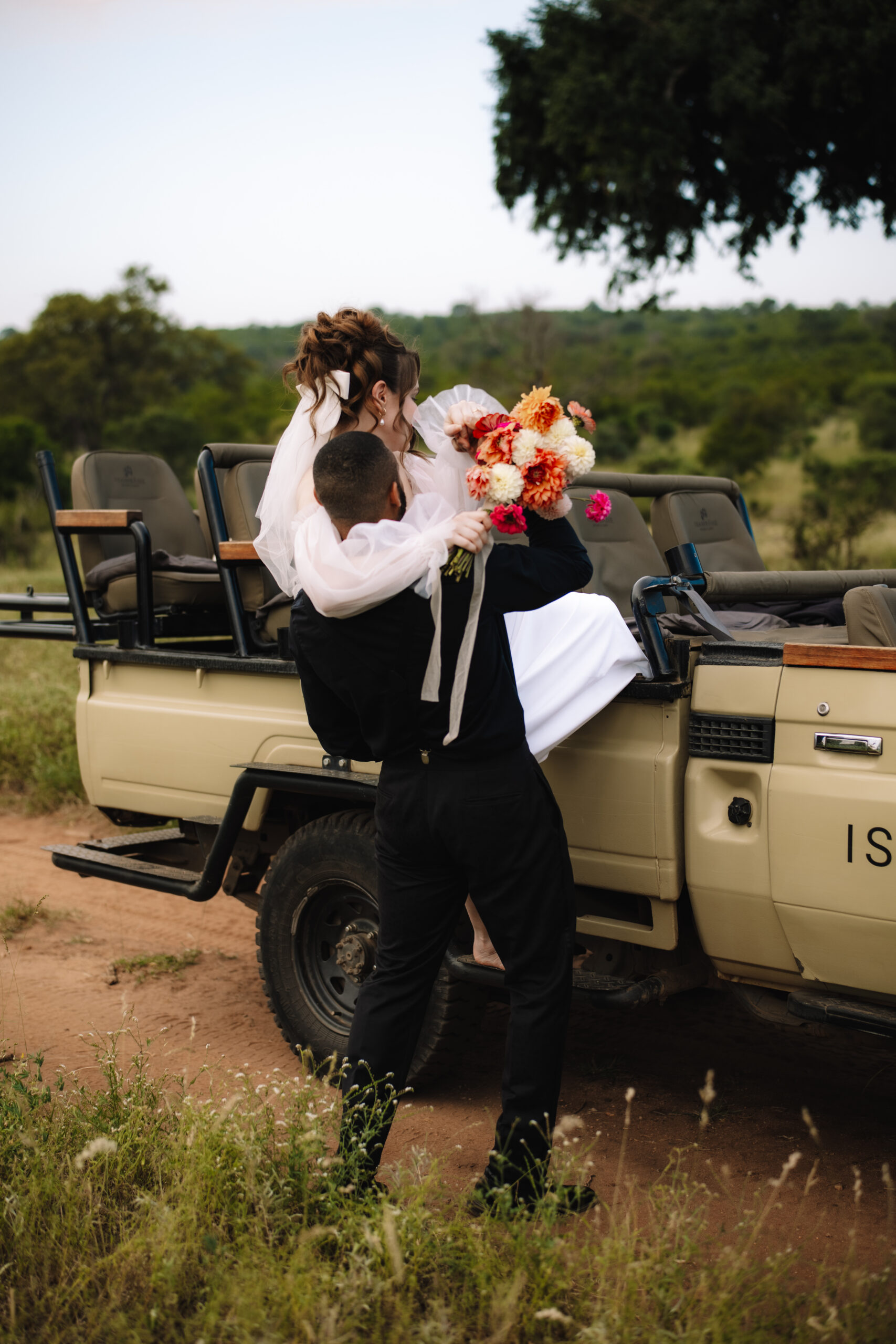 Groom lifting his bride into an open safari vehicle during their Cape Town honeymoon.