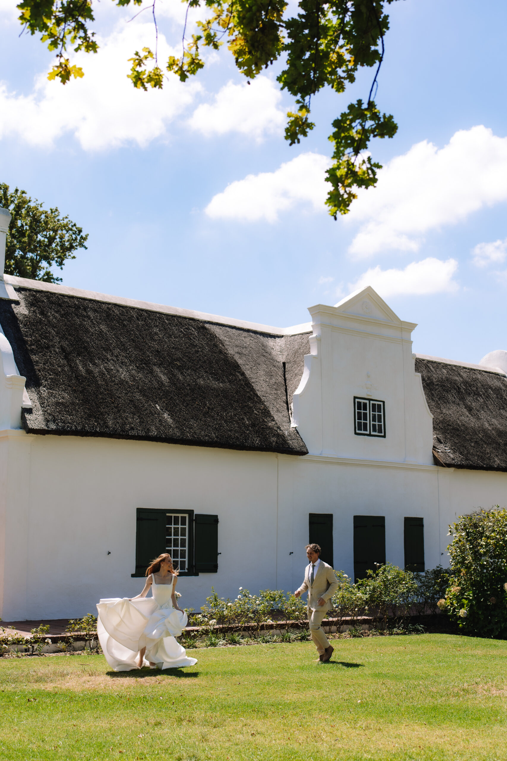Bride and groom running across the lawn of a Cape Winelands estate in South Africa.