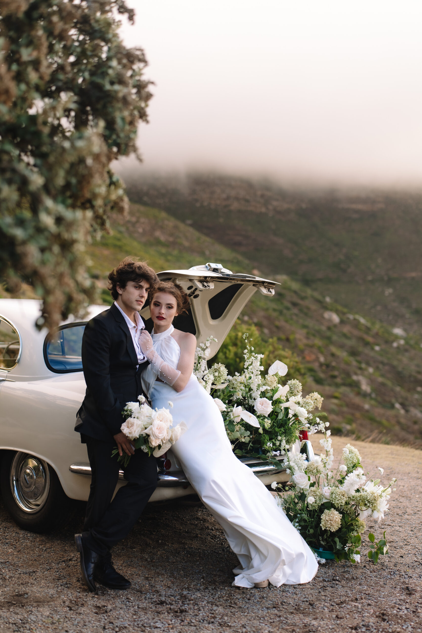 Bride and groom styled with a vintage car overlooking the mountains during their Cape Town honeymoon photoshoot.