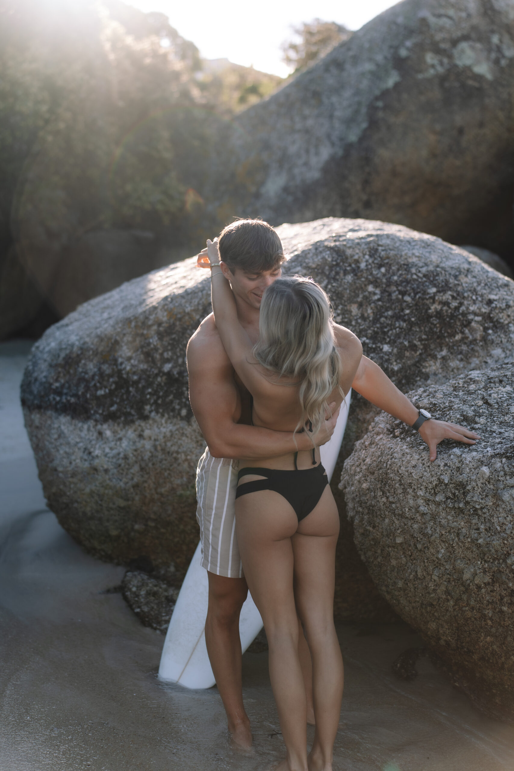 Couple embracing between coastal boulders during their Cape Town honeymoon adventure.