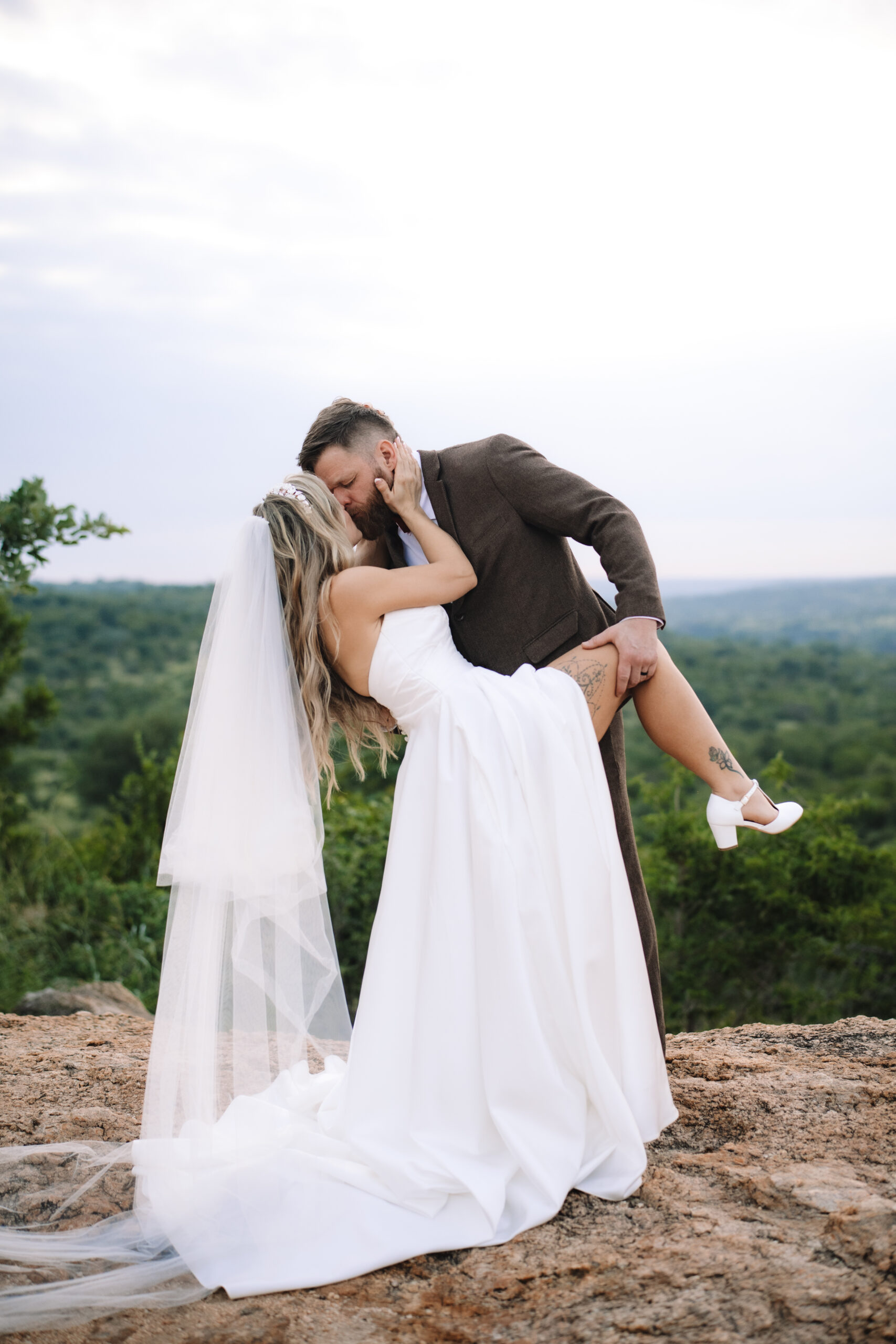 Bride and groom sharing a kiss on a rocky overlook with sweeping African landscape views during their elopement