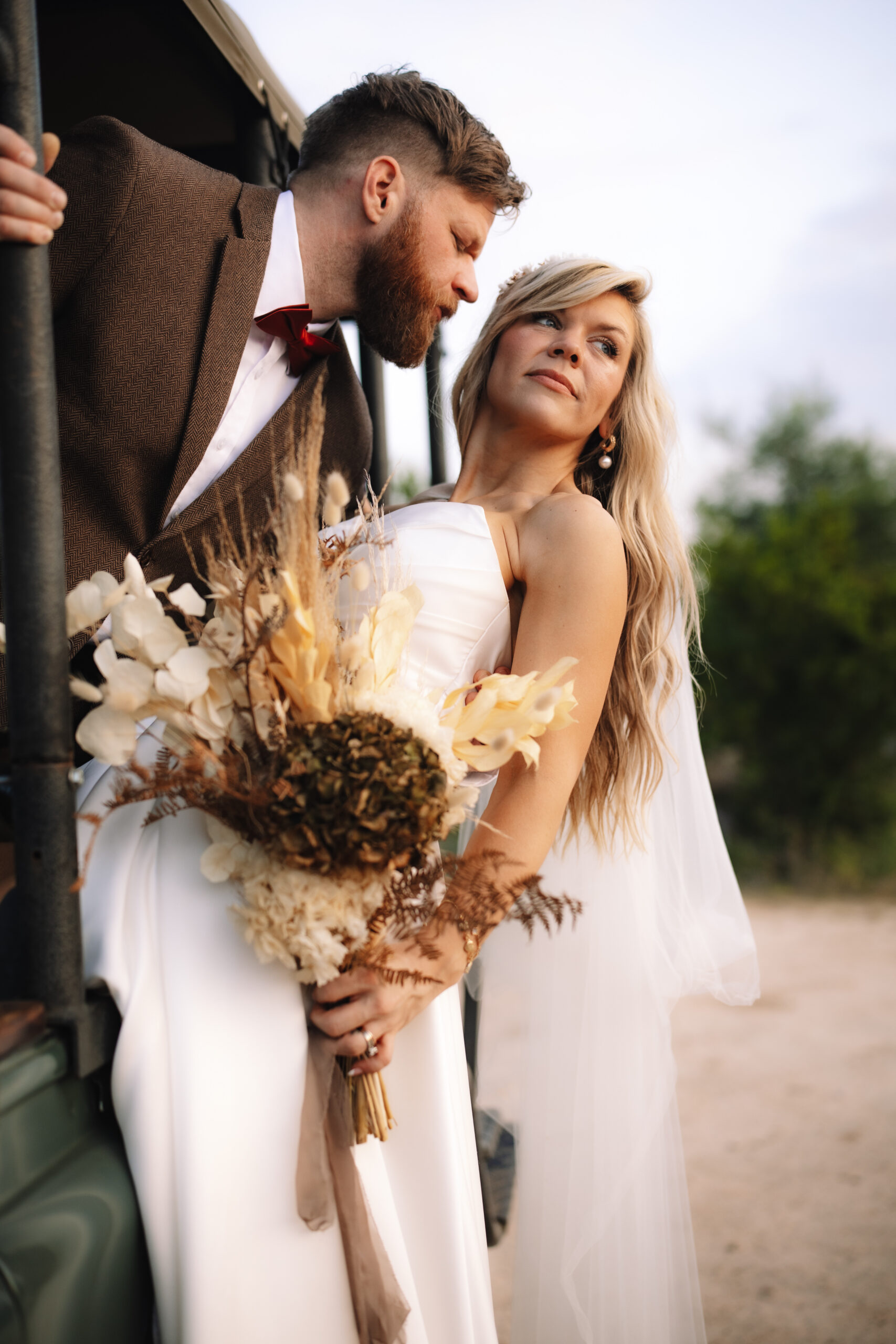 Bride and groom leaning against a safari vehicle holding a bouquet during a safari elopement in Africa