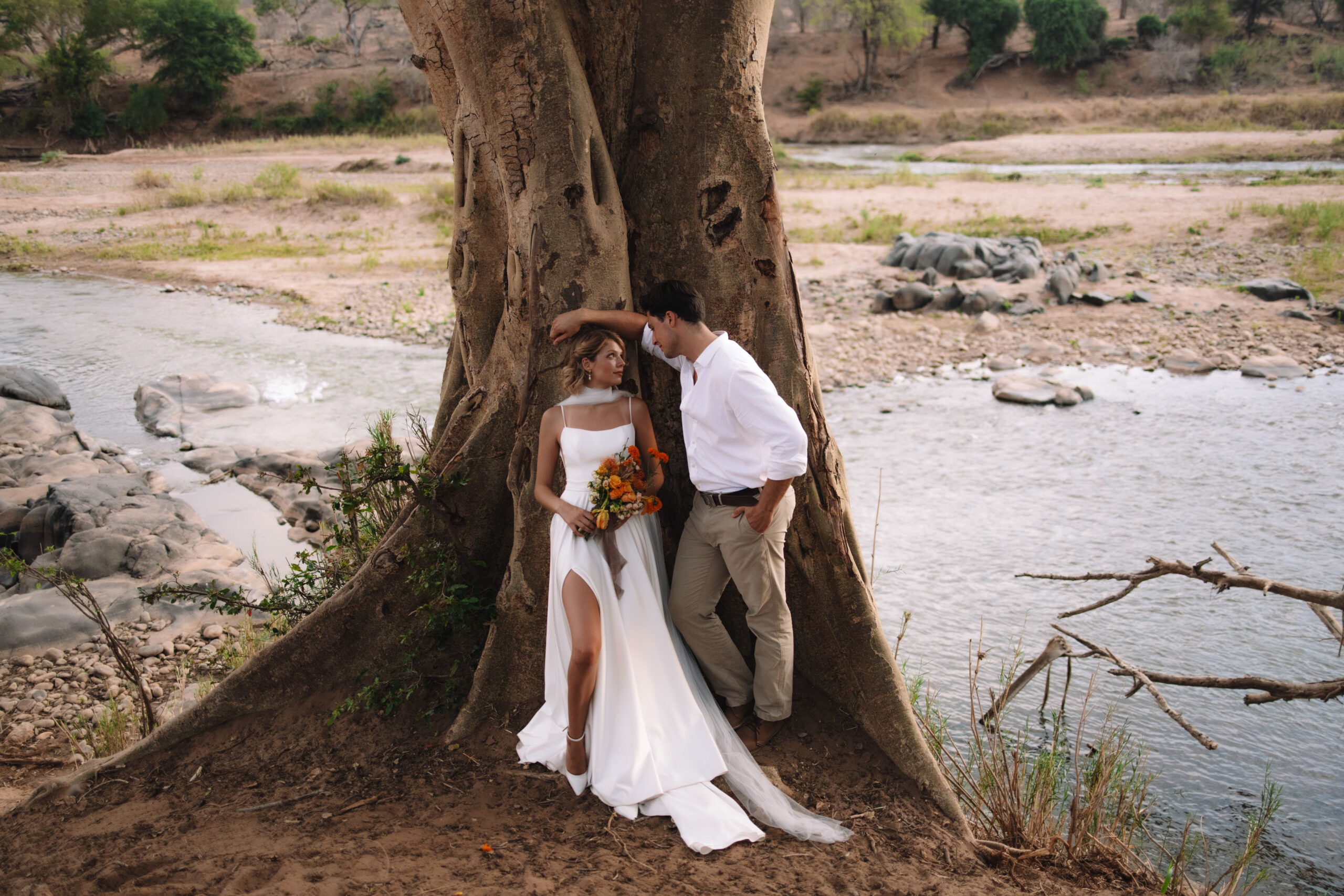 Bride and groom standing together beneath a large tree by the river during a safari elopement in Africa