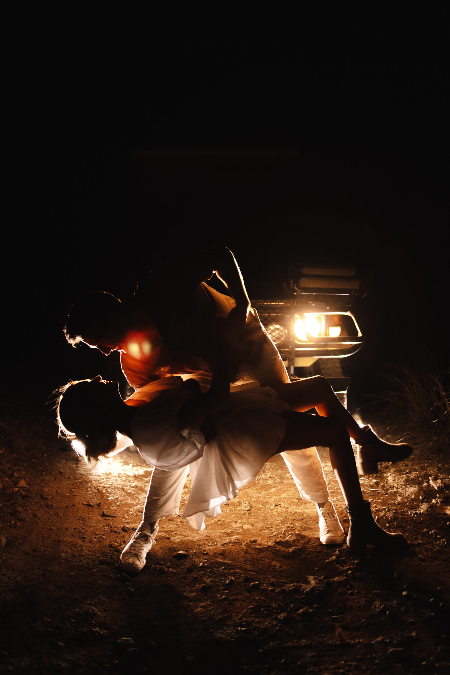 Bride and groom dancing in front of safari vehicle headlights at night after their elopement celebration
