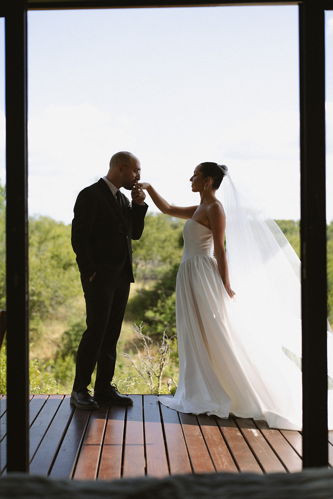 Bride holding groom’s hand as he kisses it on safari lodge deck during elopement portraits
