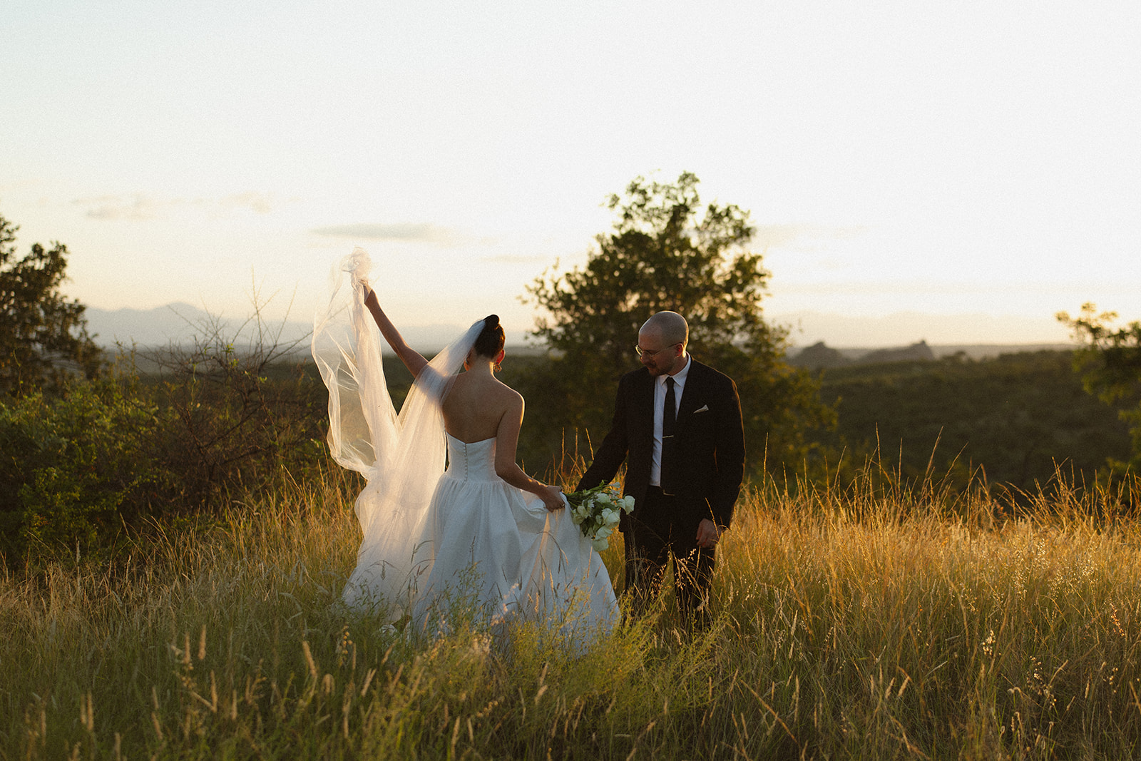 Bride lifting veil while walking through tall grass with groom after they elope in South Africa

