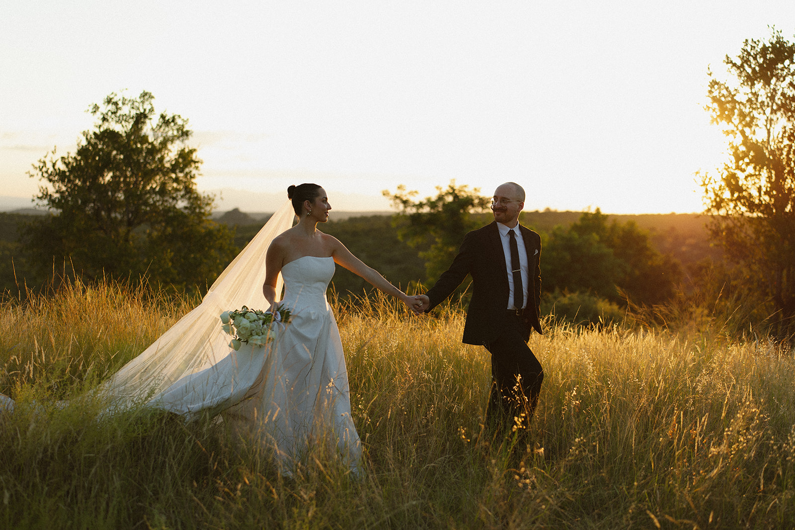 Newlyweds holding hands and walking through glowing savanna during golden hour elopement
