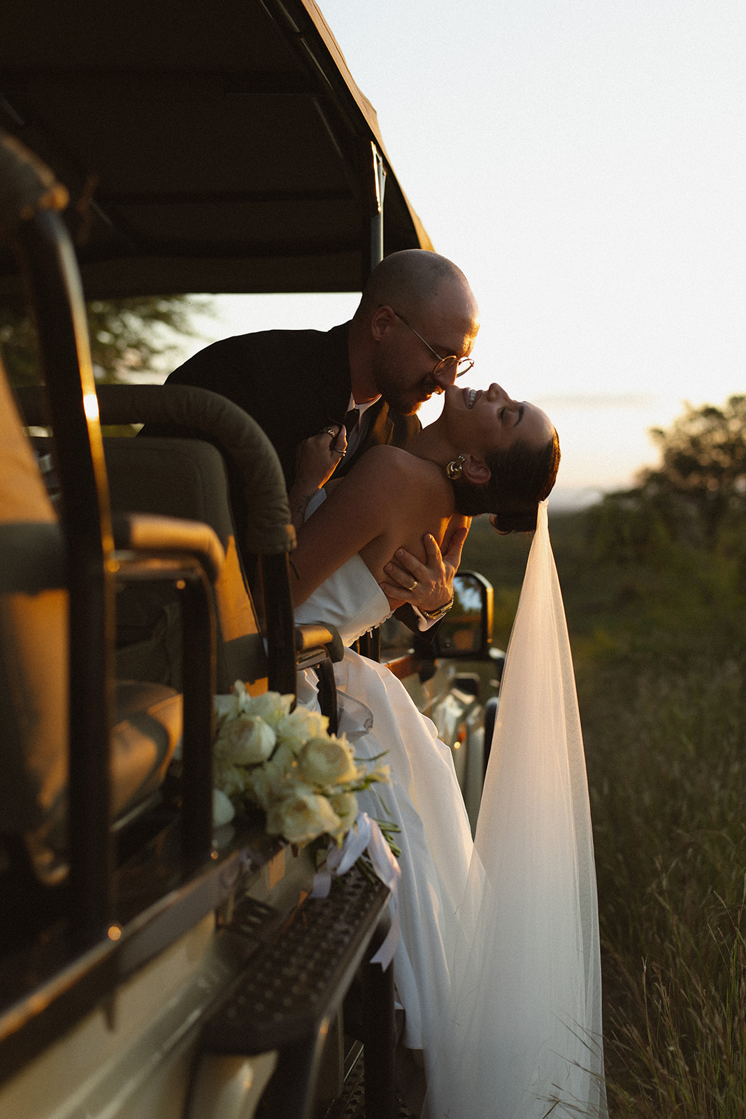 Bride leaning from safari vehicle kissing groom during golden hour after they elope in South Africa
