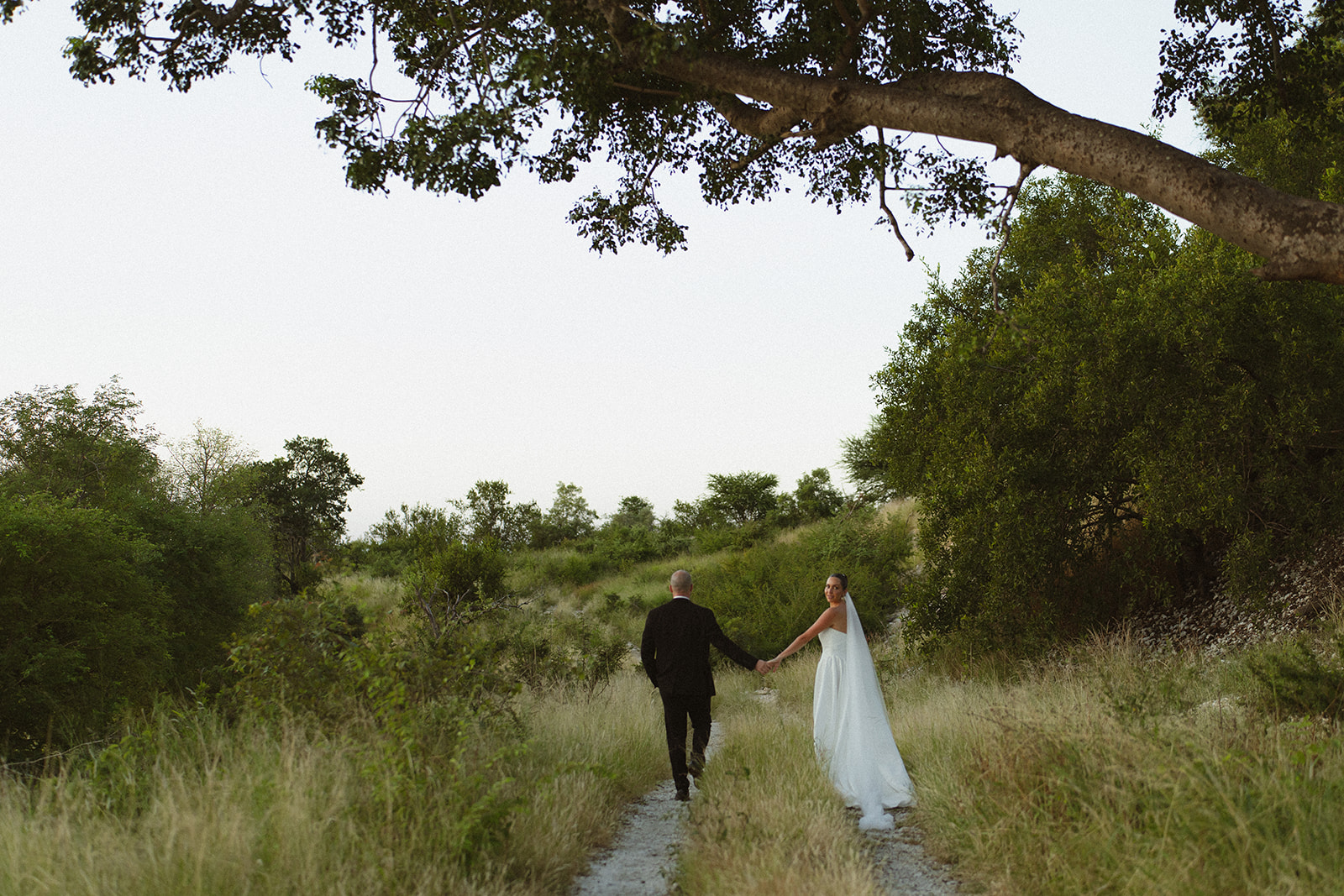 Bride and groom walking along winding path through African bush during elopement portraits
