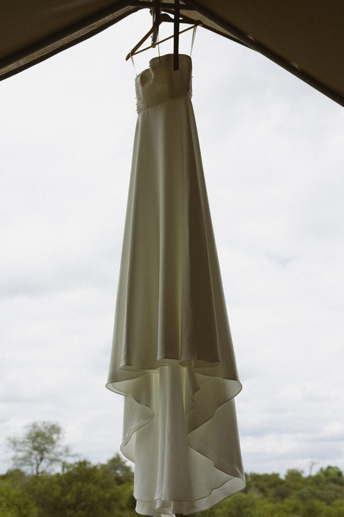 Minimal satin wedding dress hanging at safari lodge before couple elopes in South Africa

