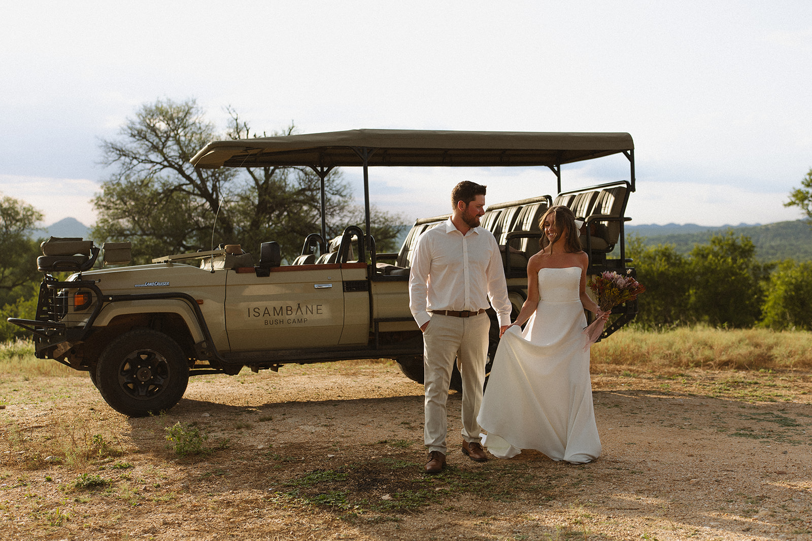 Bride and groom walking beside safari vehicle at Isambane Bush Camp after their South Africa elopement
