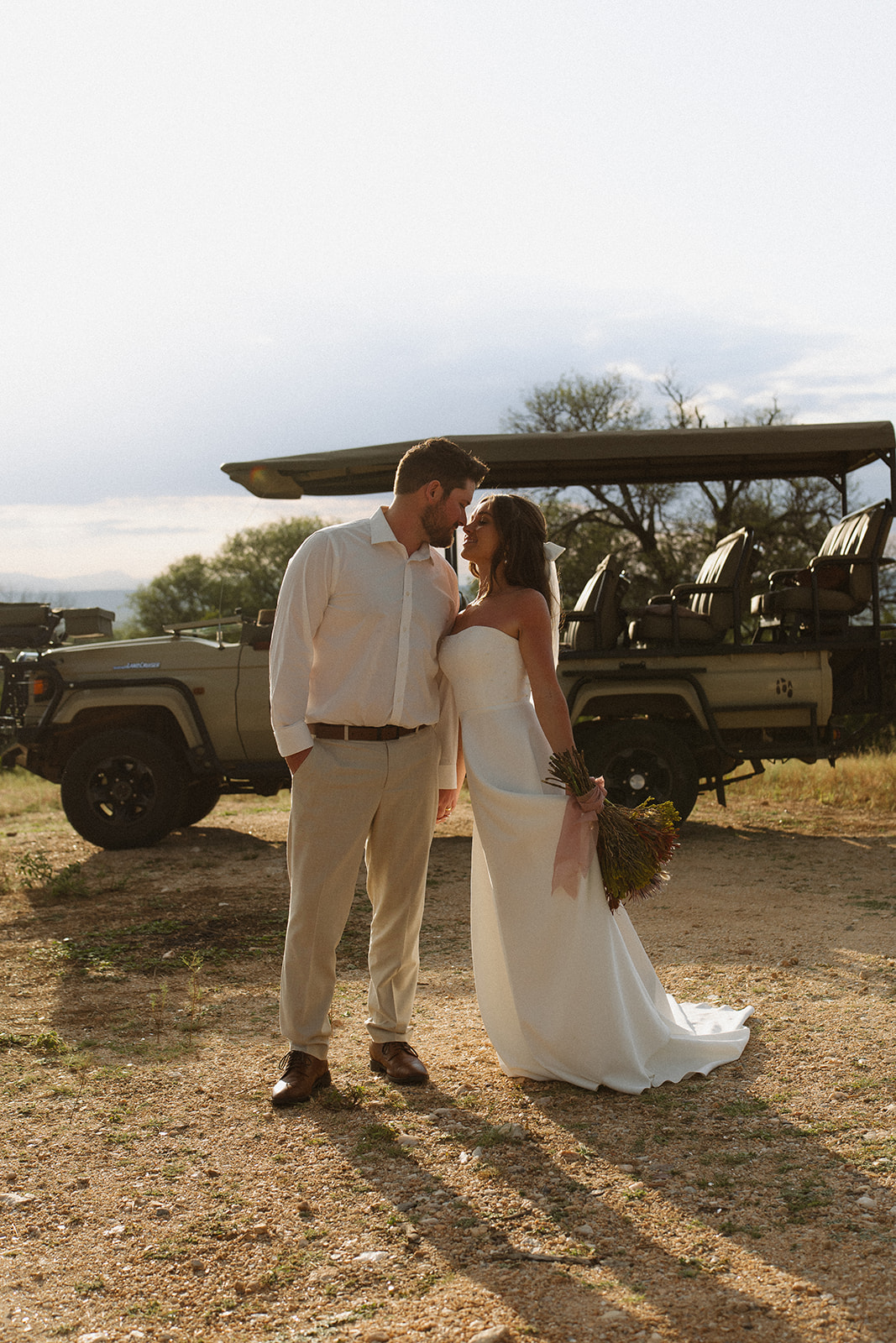 Bride and groom sharing a kiss beside safari vehicle during golden hour portraits
