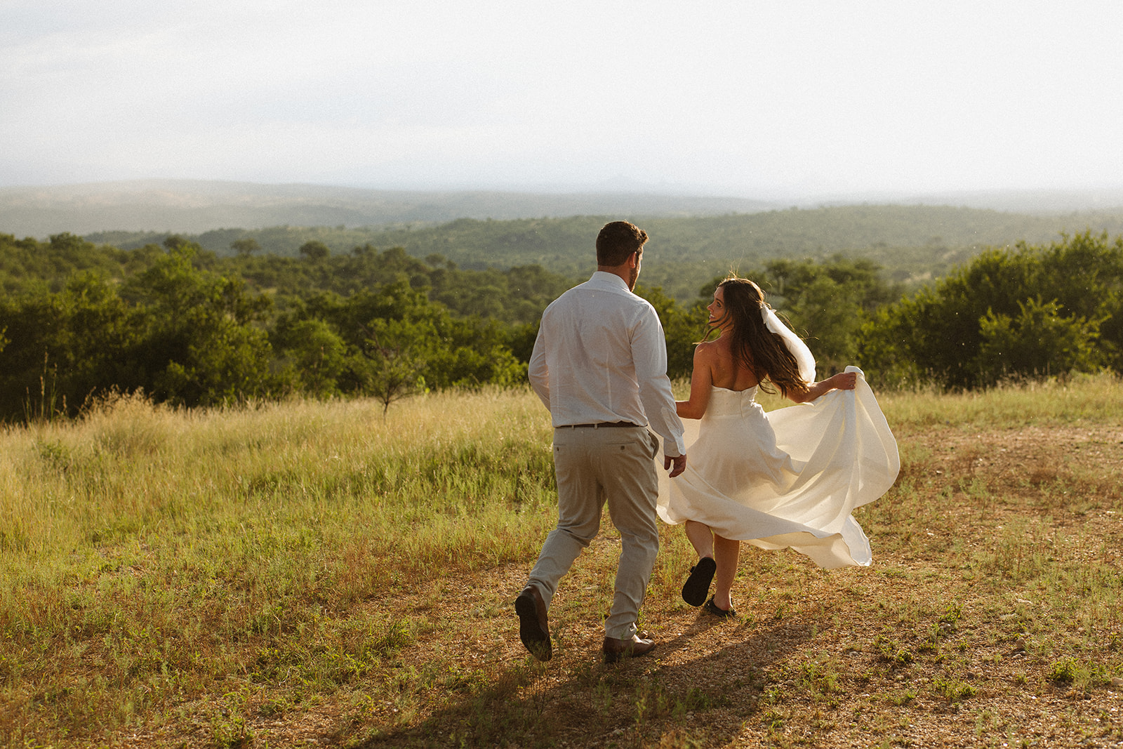 Bride and groom running through grassy savanna landscape during adventurous safari elopement
