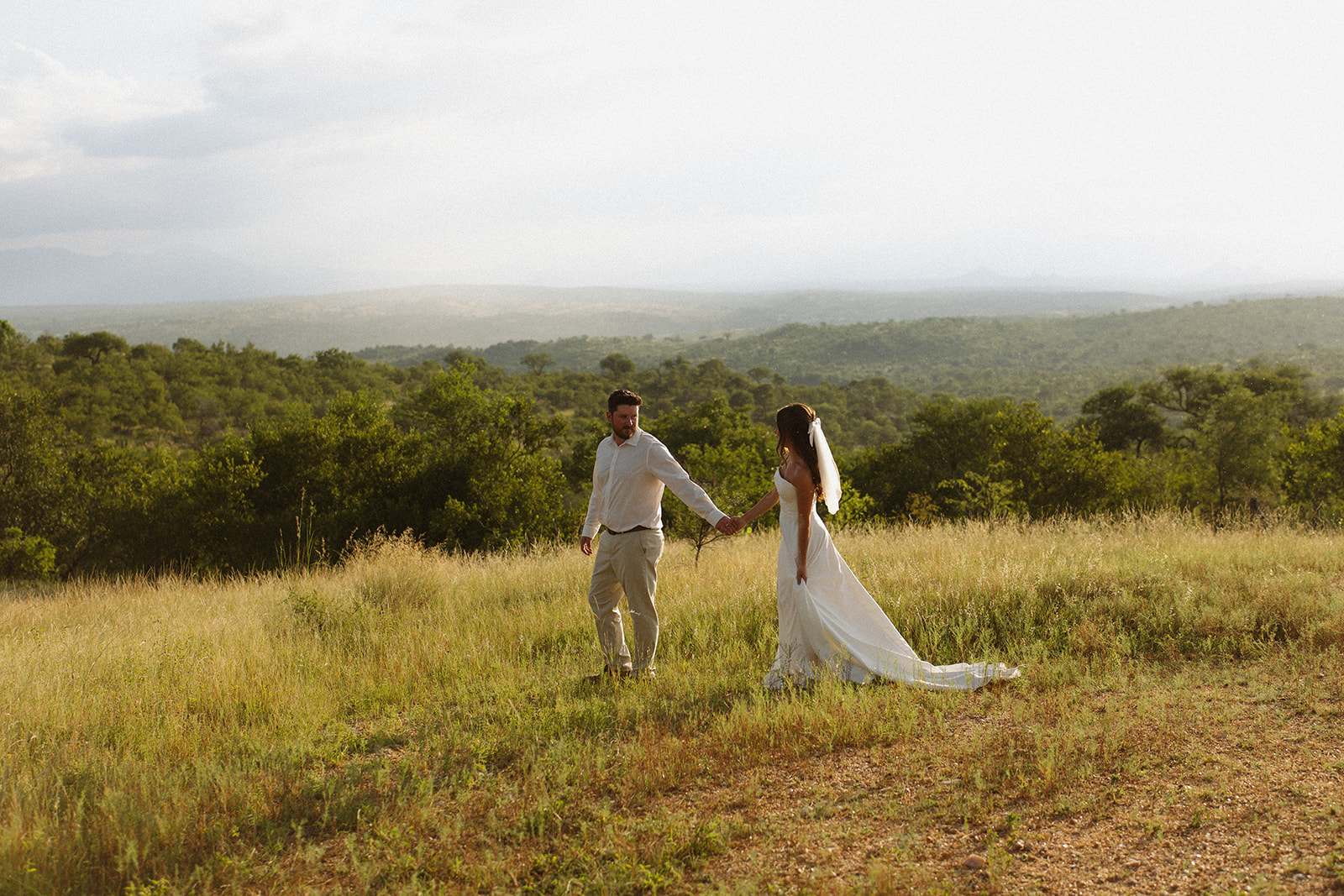 Bride and groom walking through golden savanna landscape after they elope in South Africa
