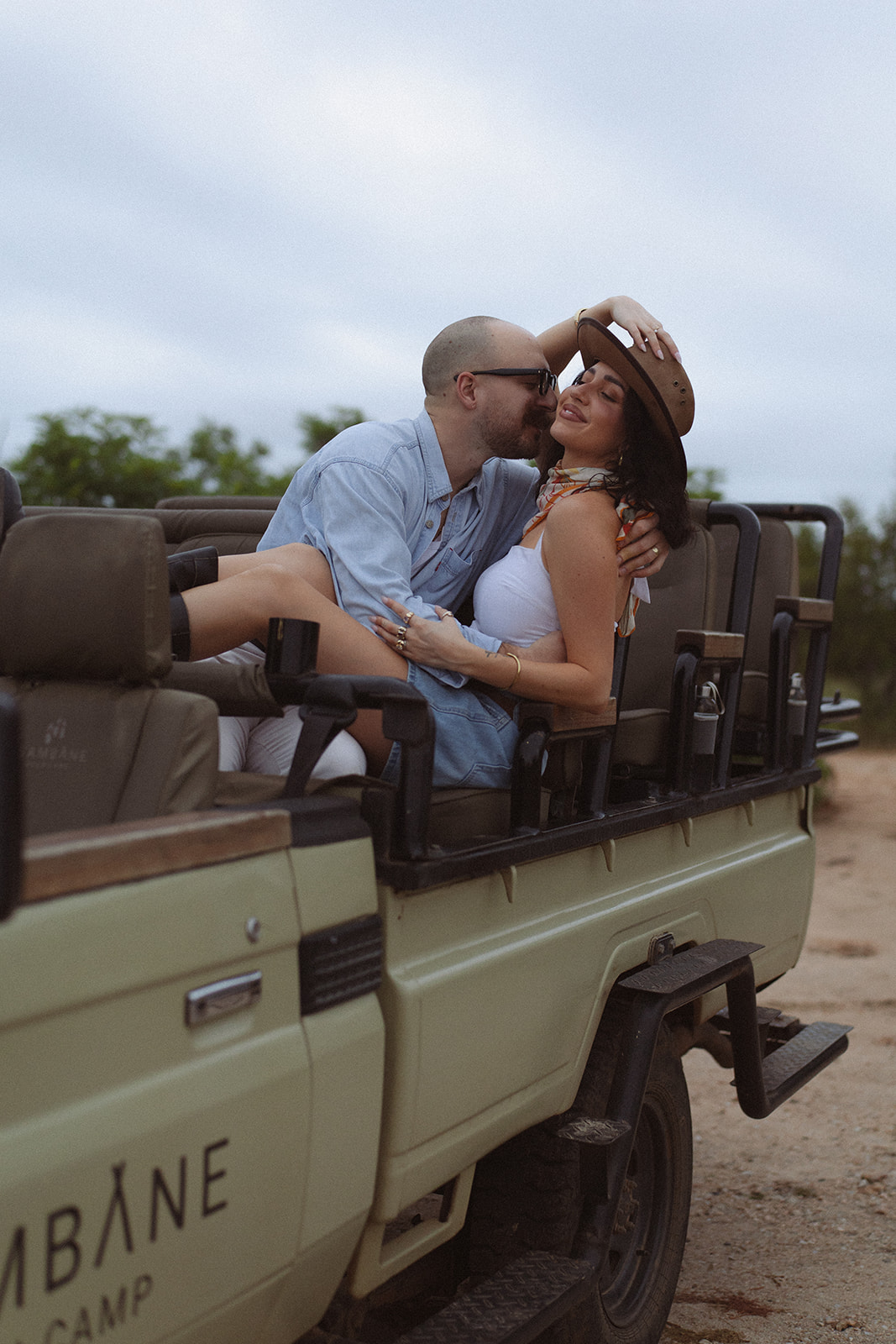 Newlywed couple kissing in an open safari vehicle during their adventure honeymoon following their Africa weddings celebration.
