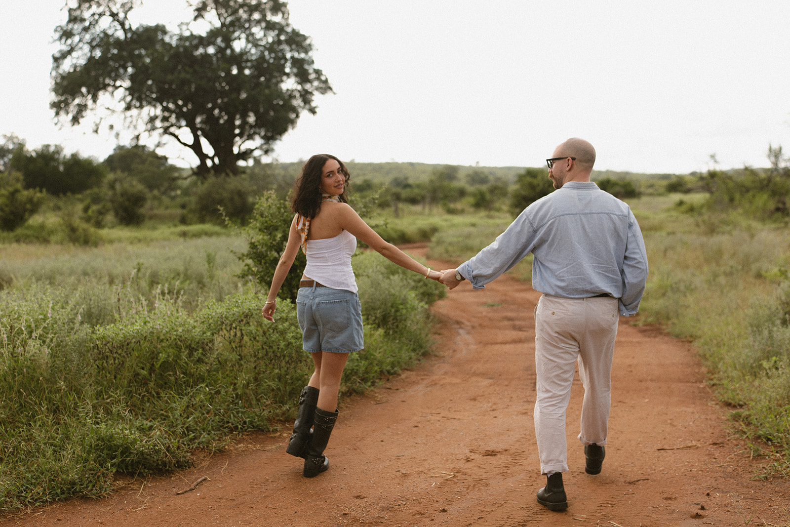 Couple holding hands and walking down a red dirt road during a safari adventure session following their Africa weddings celebration.
