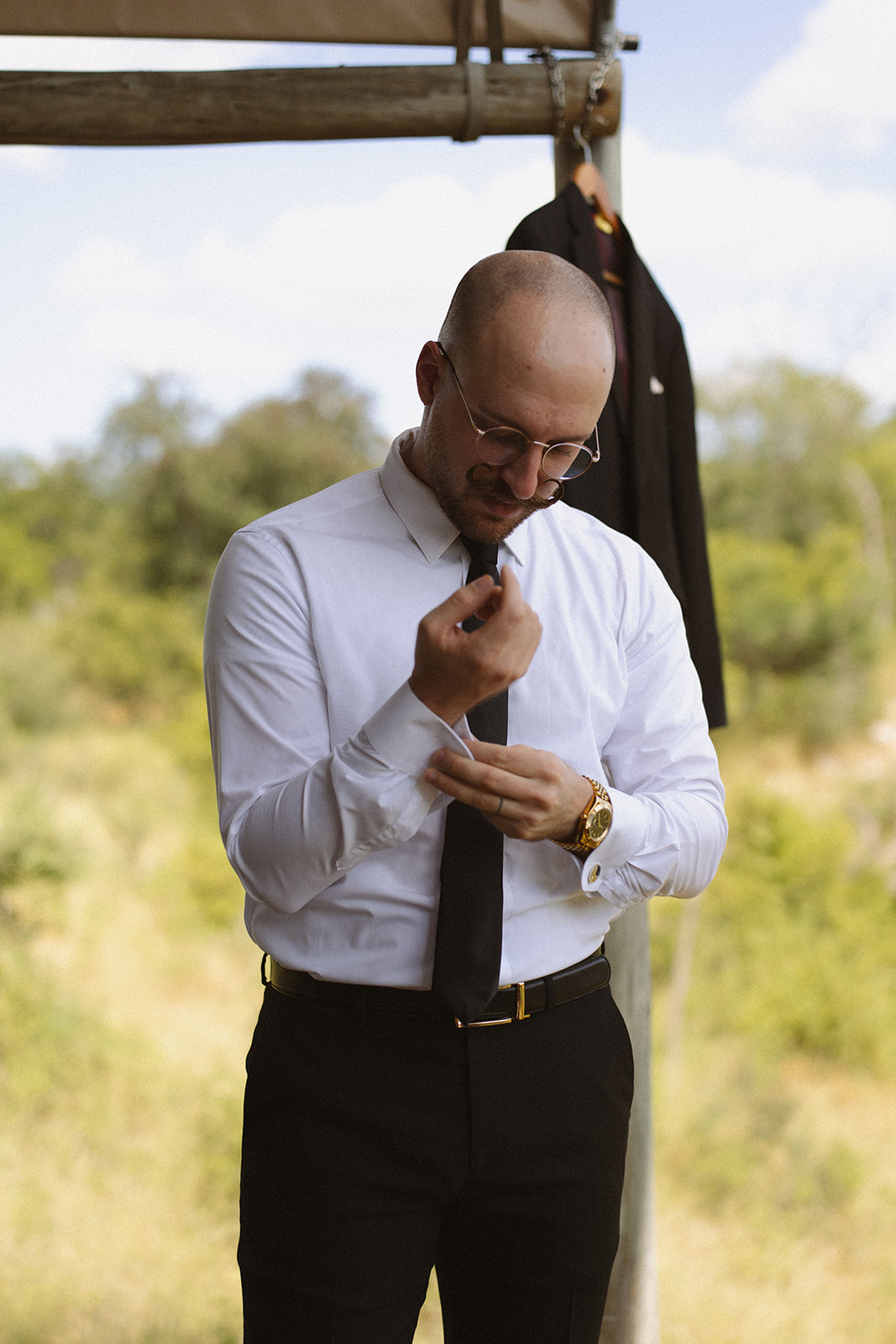 Groom adjusting his tie outdoors before the ceremony during a destination wedding in the African bush.
