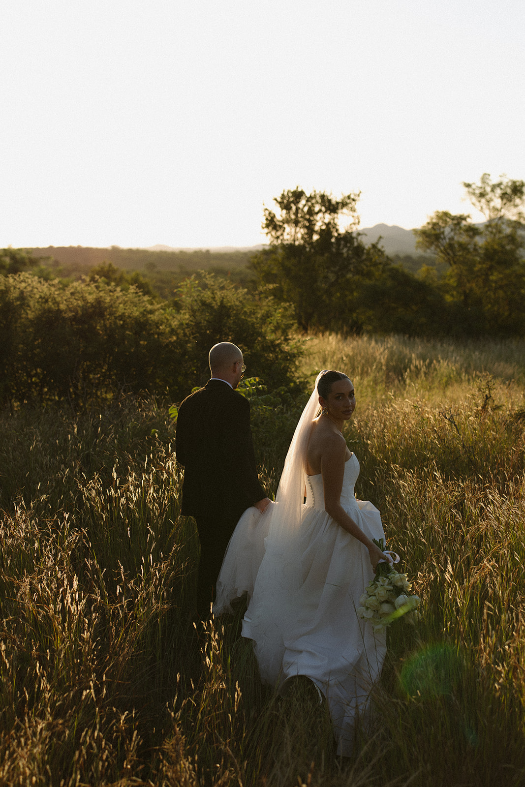 Bride and groom walking through tall golden grass at sunset during intimate Africa weddings portraits in South Africa.
