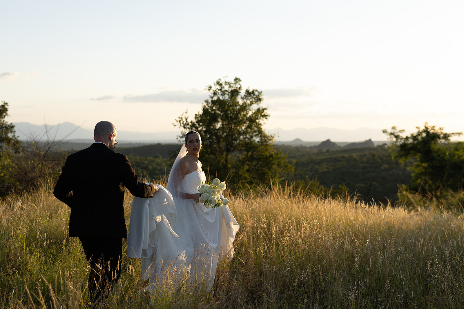 Bride and groom walking through golden savanna grass during sunset wedding portraits in South Africa.
