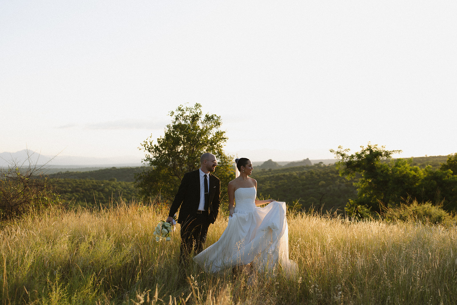 Bride and groom walking through tall golden grass at sunset during stunning portrait time for Africa weddings.
