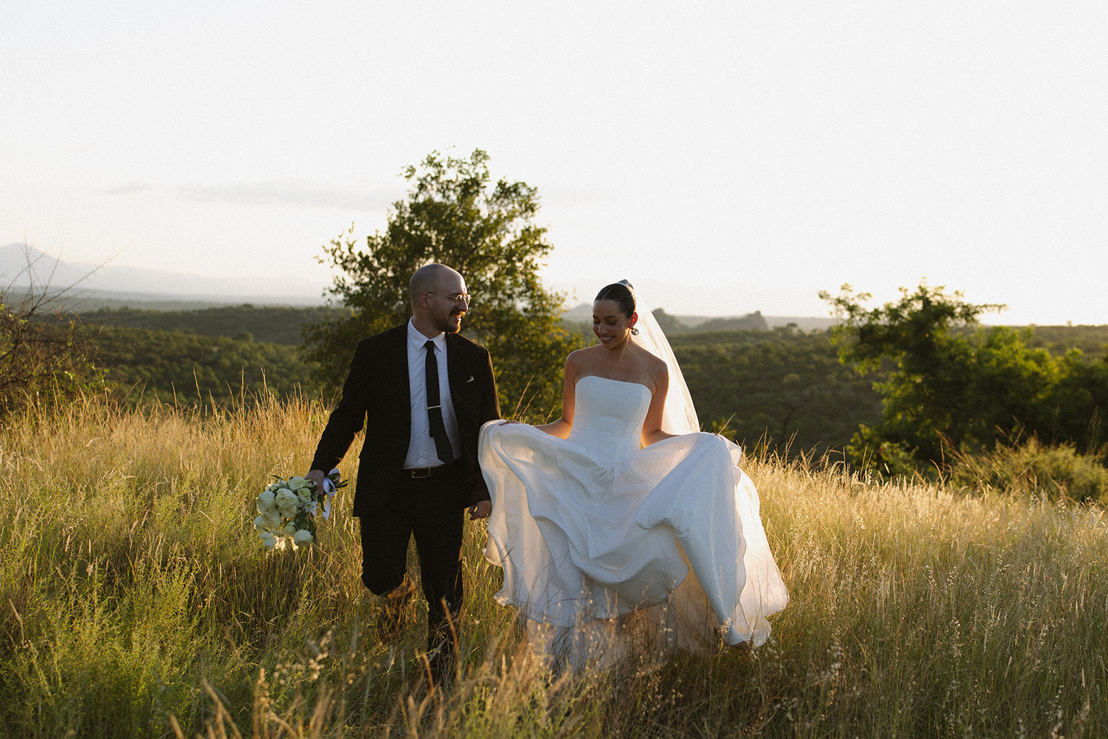 Bride and groom walking through golden grass at sunset holding hands during romantic Africa weddings portraits.
