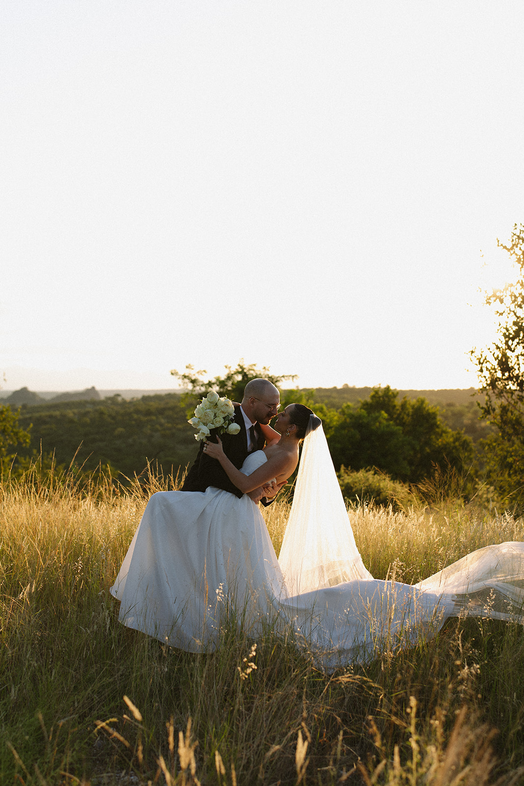 Groom dipping his bride in tall golden grass during dreamy golden hour portraits for Africa weddings.
