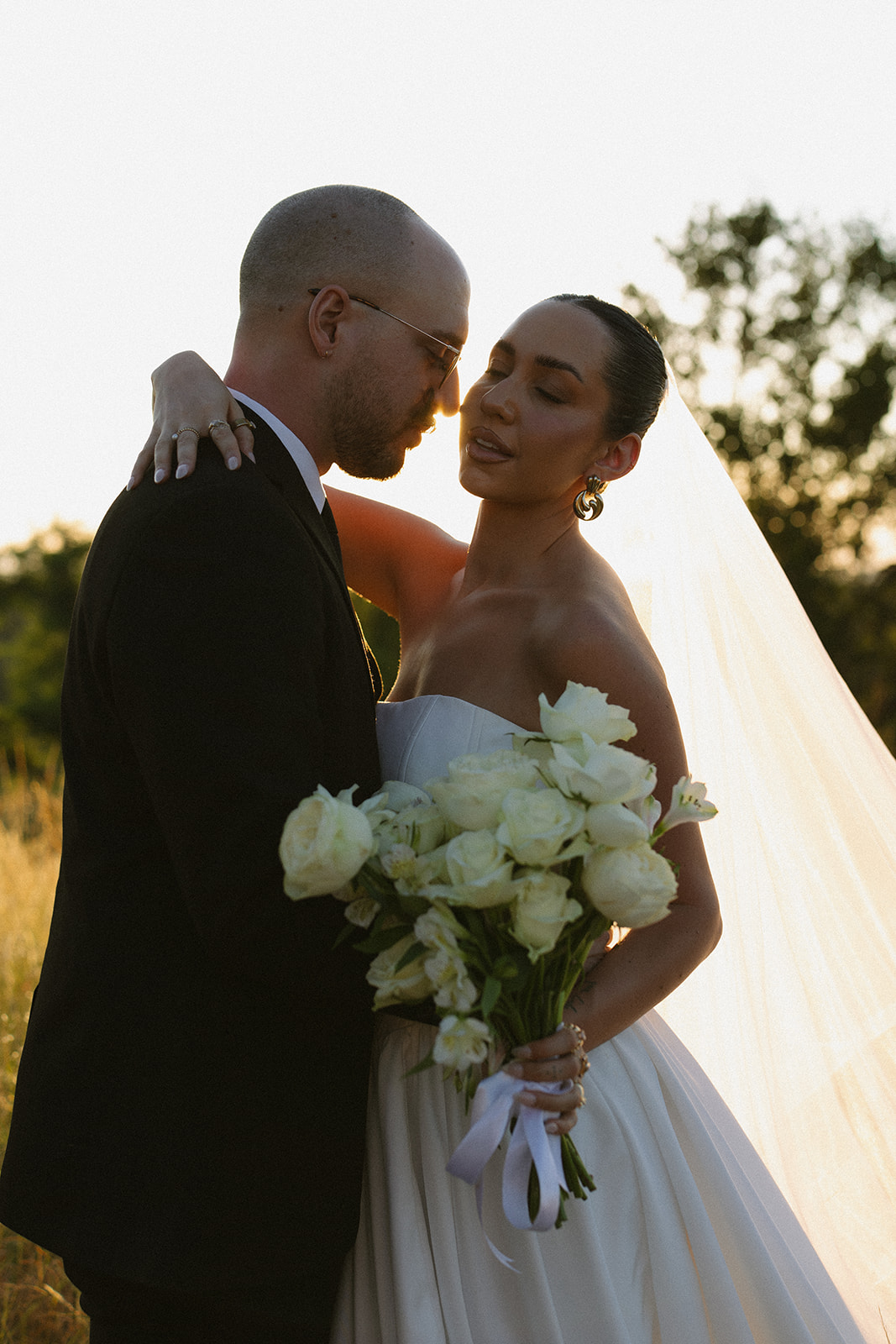 Bride and groom embracing at sunset with bouquet of white roses during dreamy golden hour portraits for Africa weddings.
