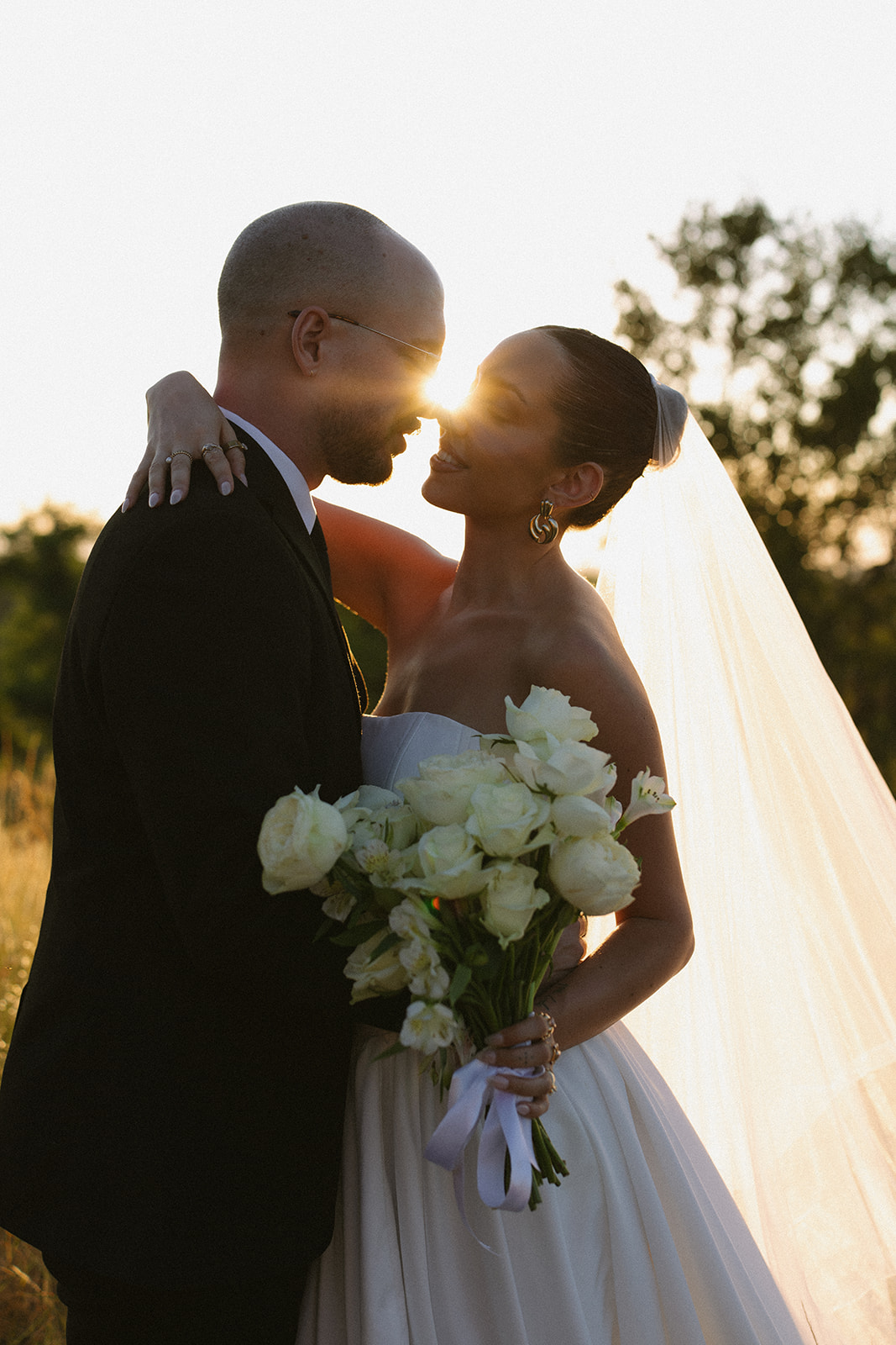 Romantic sunset portrait of bride and groom embracing with a bouquet of white roses during a destination wedding in Africa.
