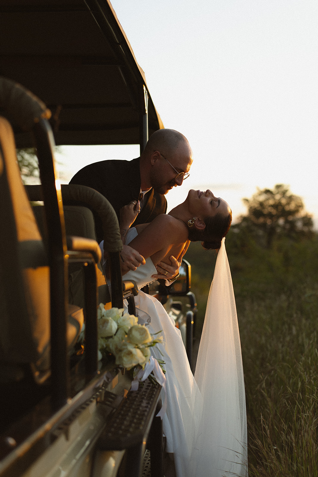 Groom dipping his bride beside a safari vehicle at sunset during romantic Africa weddings portraits in the savanna.
