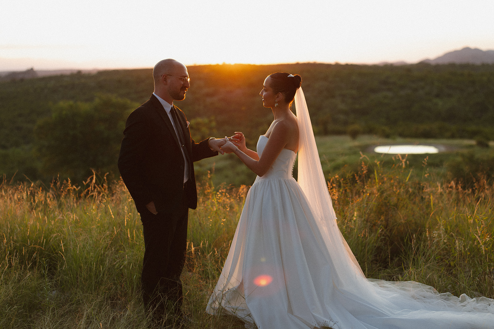 Bride and groom exchanging rings in tall golden grass at sunset during an intimate Africa weddings ceremony.
