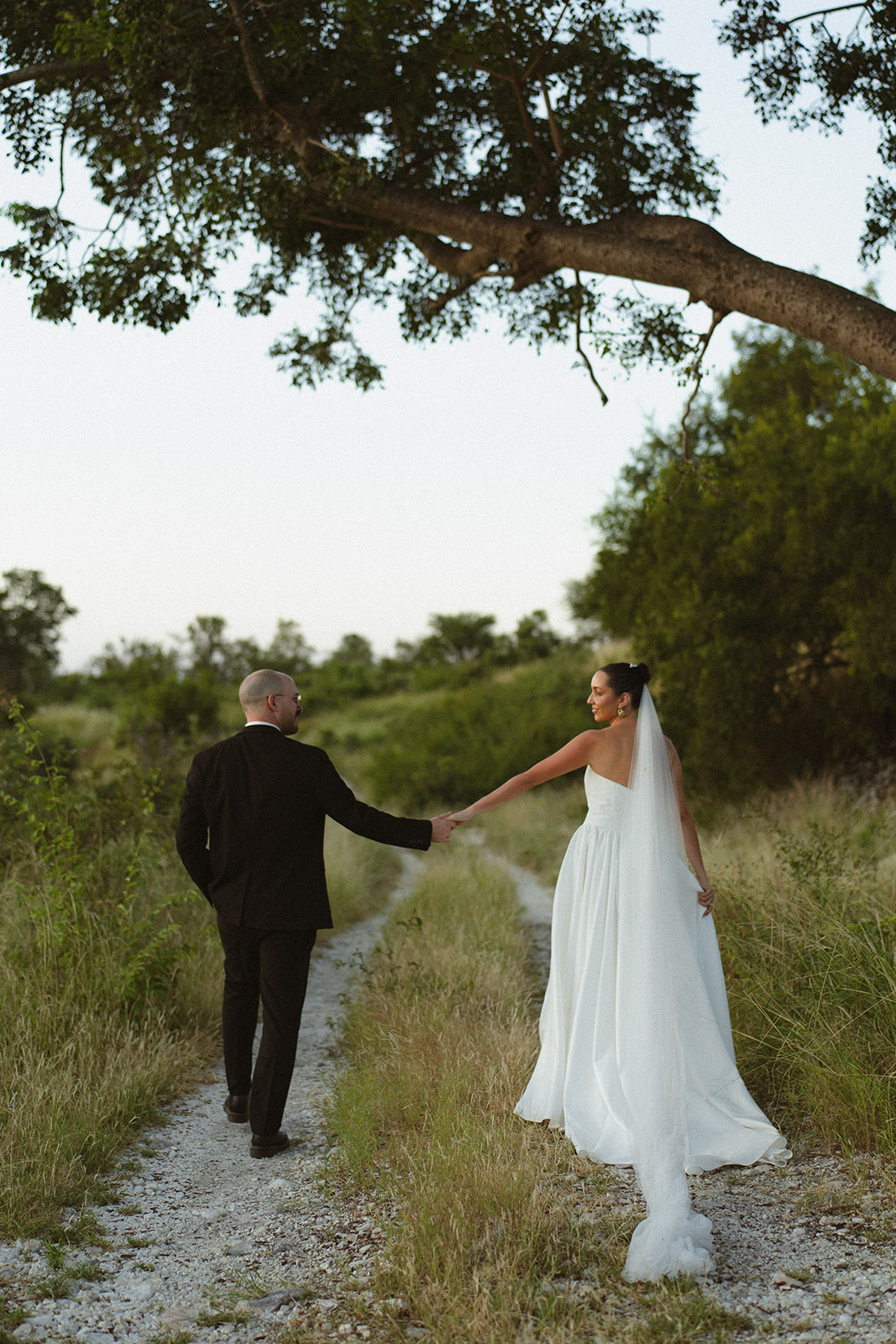 Bride and groom walking hand in hand down a scenic path beneath a large tree during an intimate Africa weddings portrait session.
