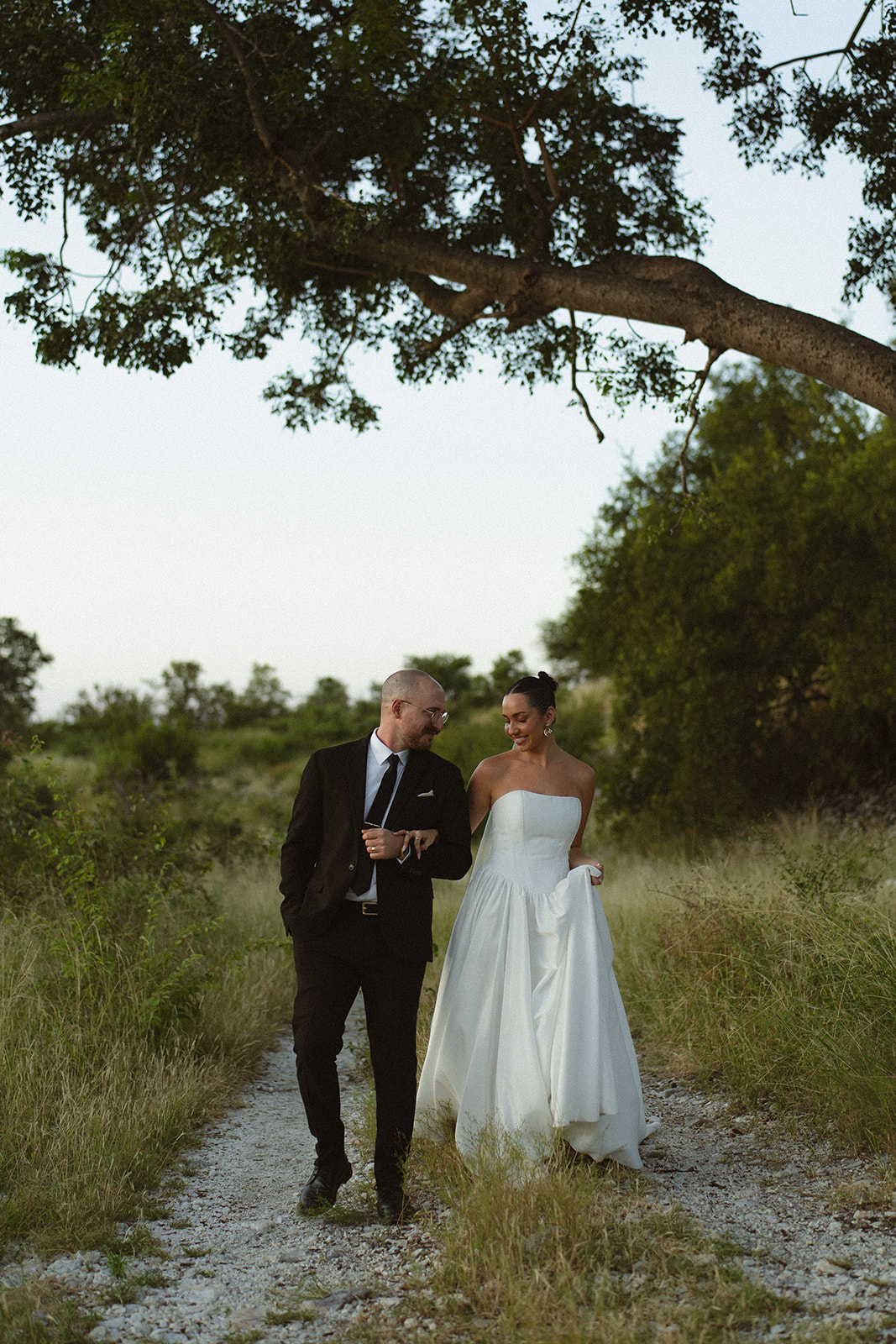 Newlywed couple walking together along a path under a large tree during an intimate safari lodge wedding in Africa.
