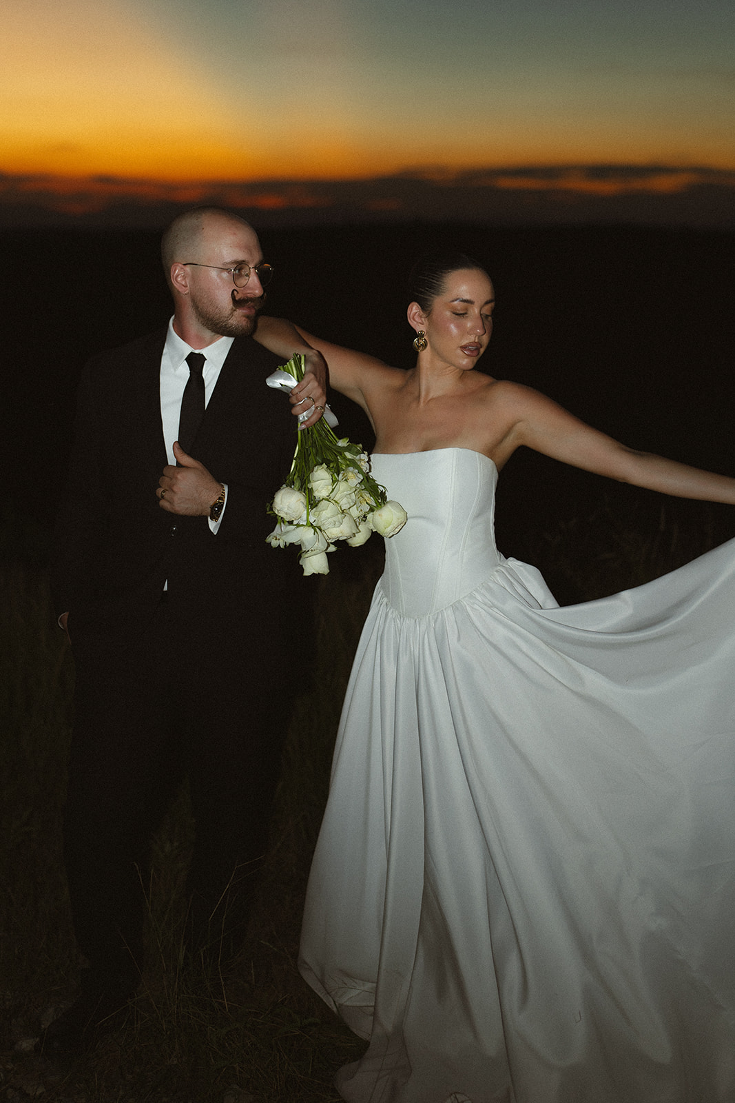 Elegant nighttime portrait of bride and groom with flowing wedding dress and bouquet during a destination wedding in Africa.

