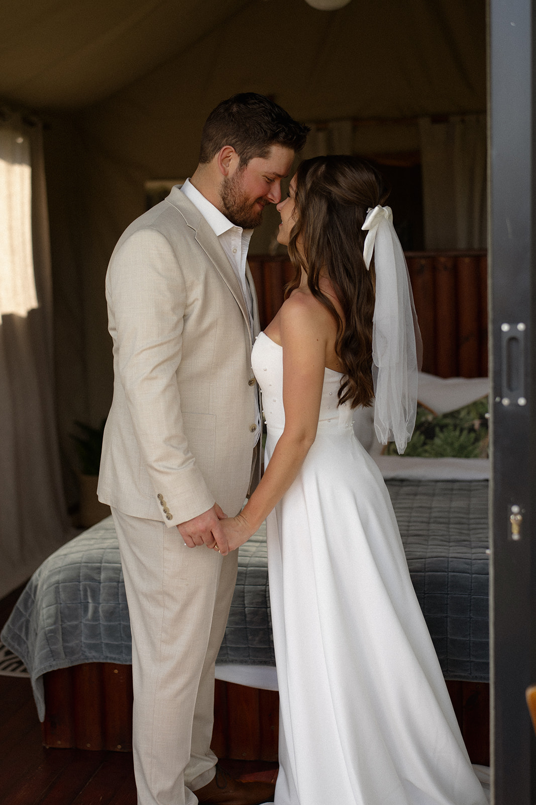 Bride and groom sharing an intimate moment inside a safari lodge bedroom filled with soft natural light
