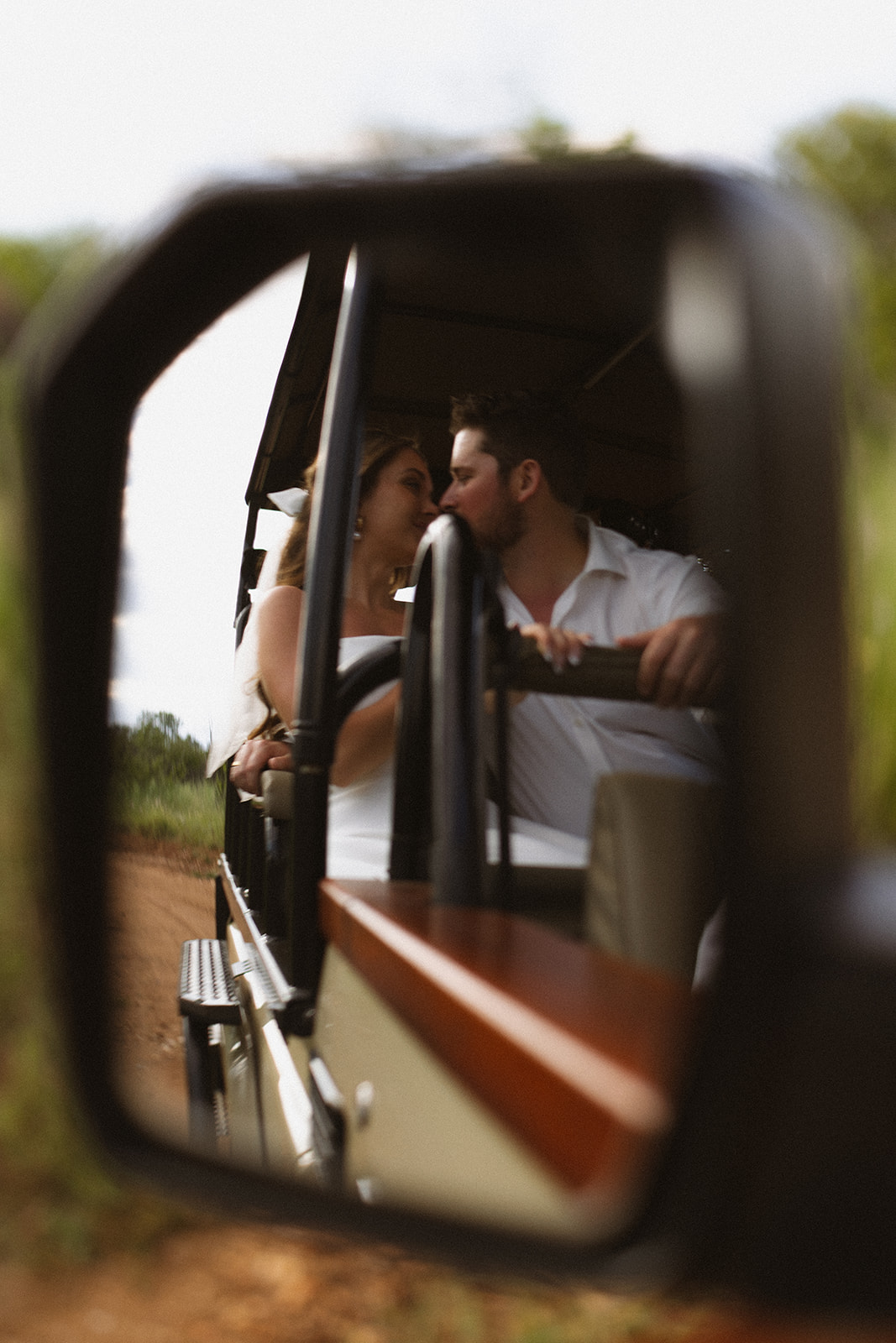 Bride and groom kissing reflected in safari vehicle mirror during a candid wedding moment
