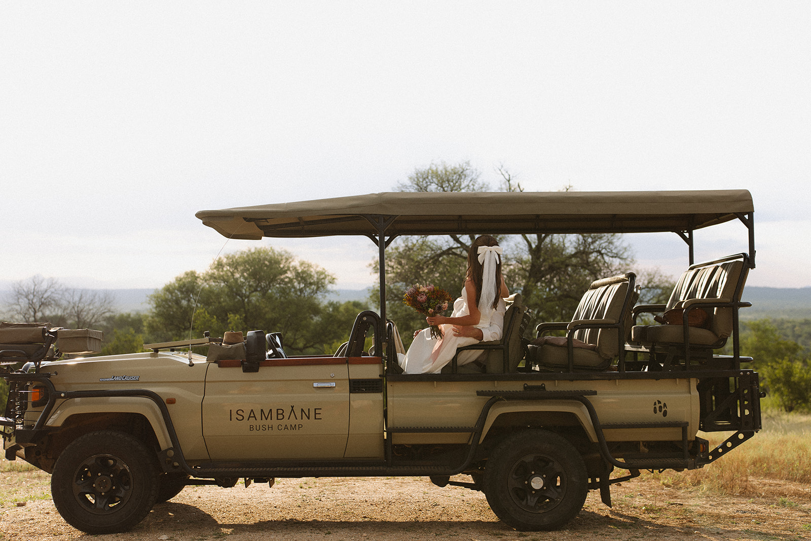 Bride sitting in an open-air safari vehicle overlooking the African landscape, part of a luxury safari wedding packages experience
