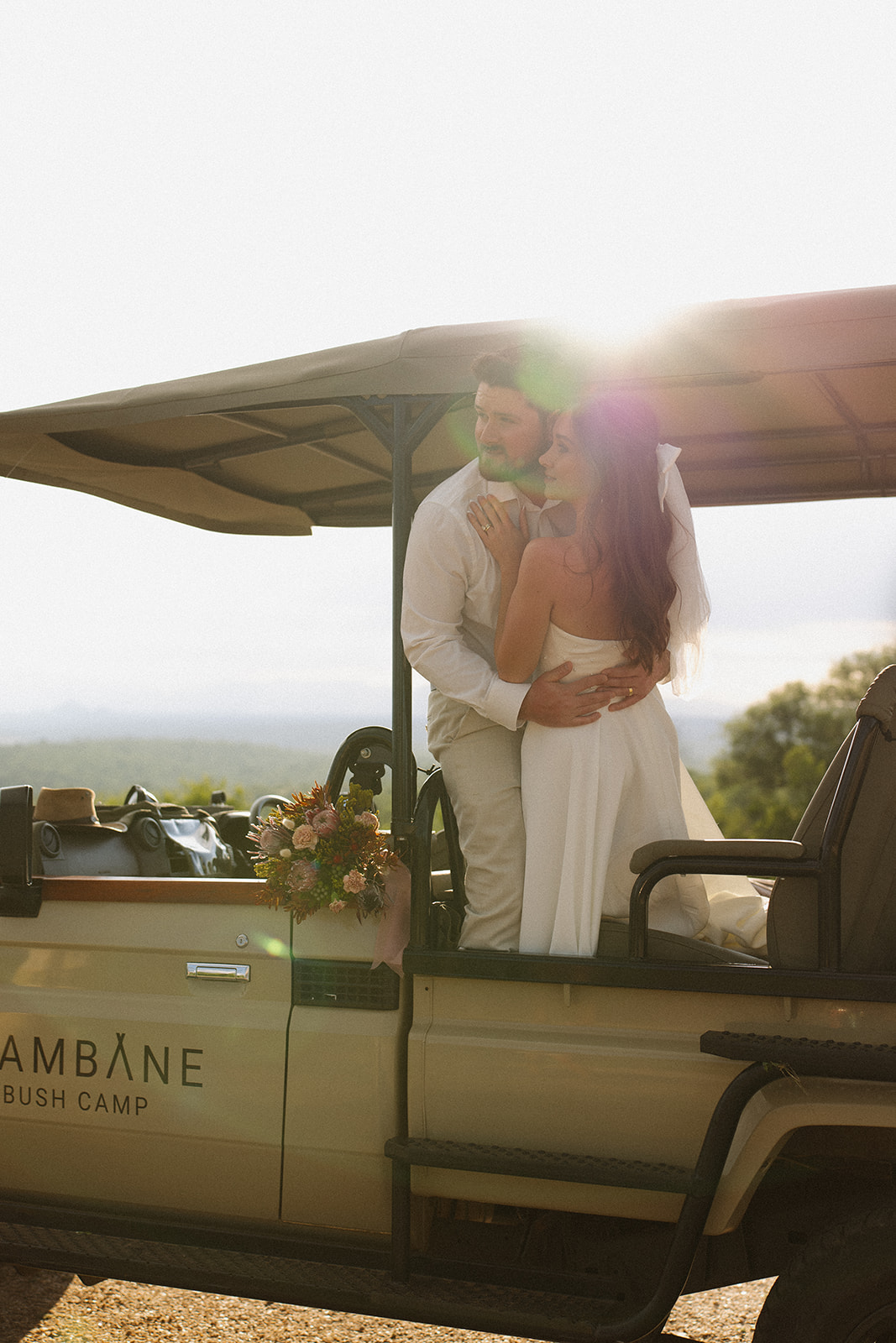Bride and groom embracing on safari vehicle with soft sun flare during a romantic safari wedding packages moment
