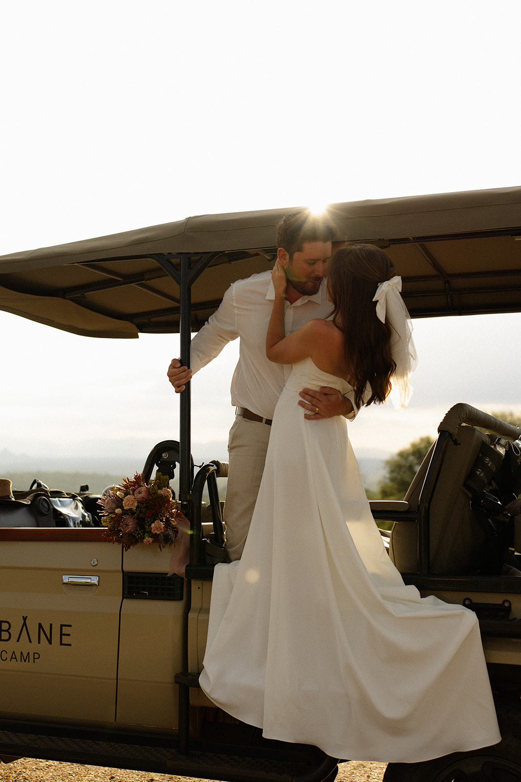 Bride and groom embracing on safari jeep with bouquet and glowing sunset light during a safari wedding packages experience
